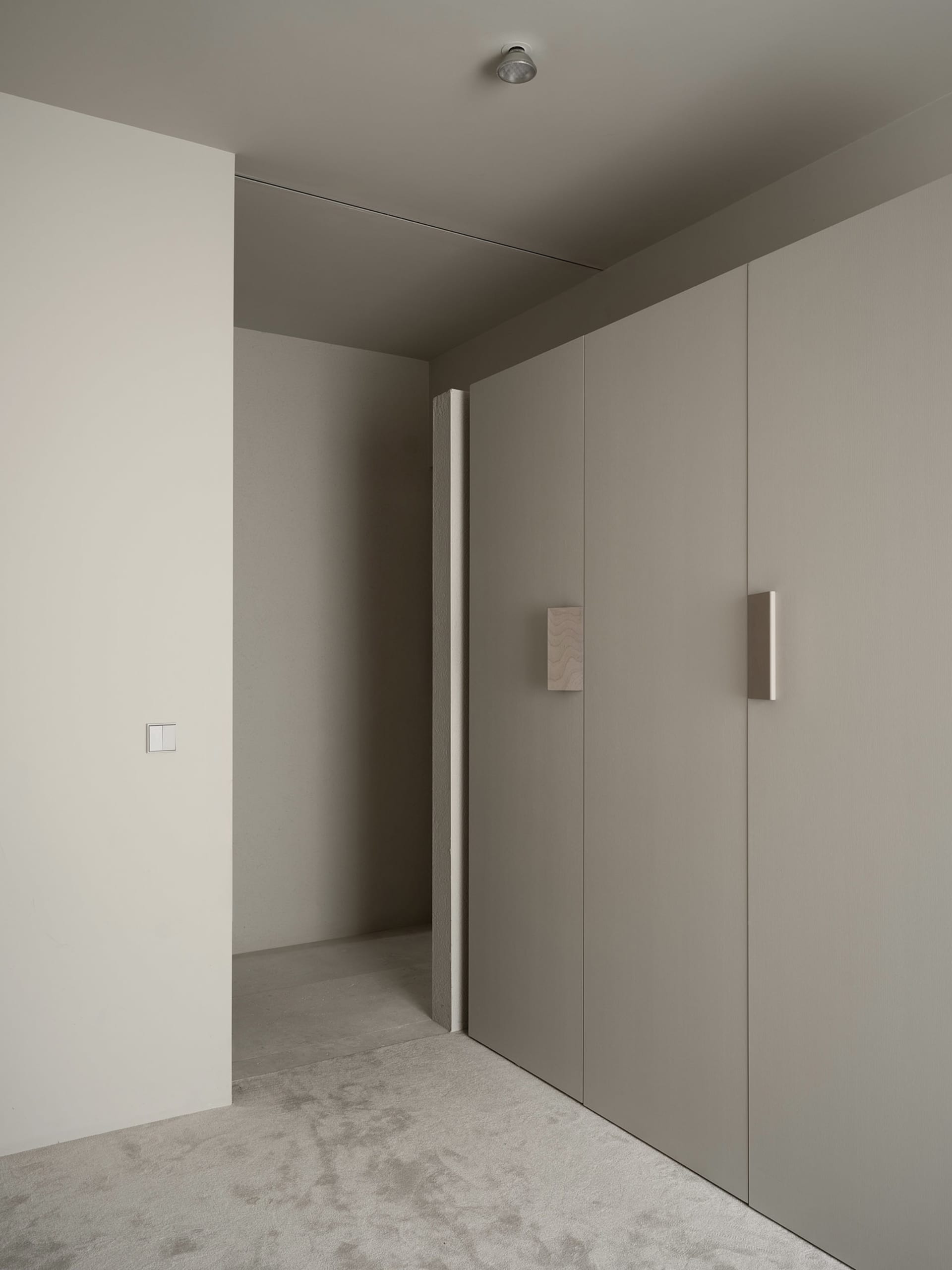 A dimly lit gray hallway with concrete walls and white surfaces, featuring a doorway