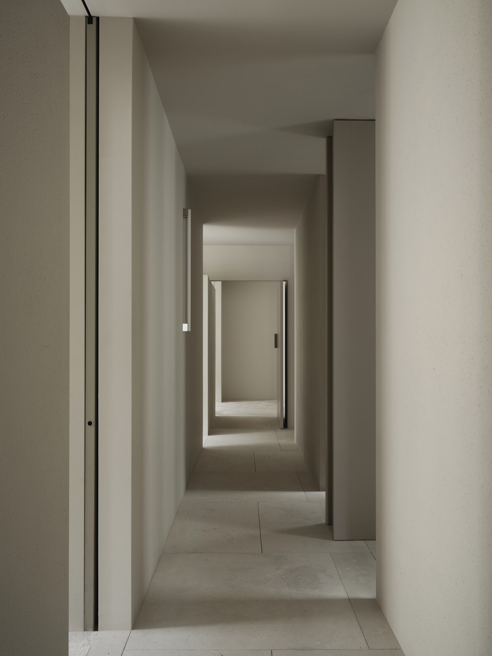 A dimly lit, narrow hallway with a concrete floor and walls, featuring a doorway at the end
