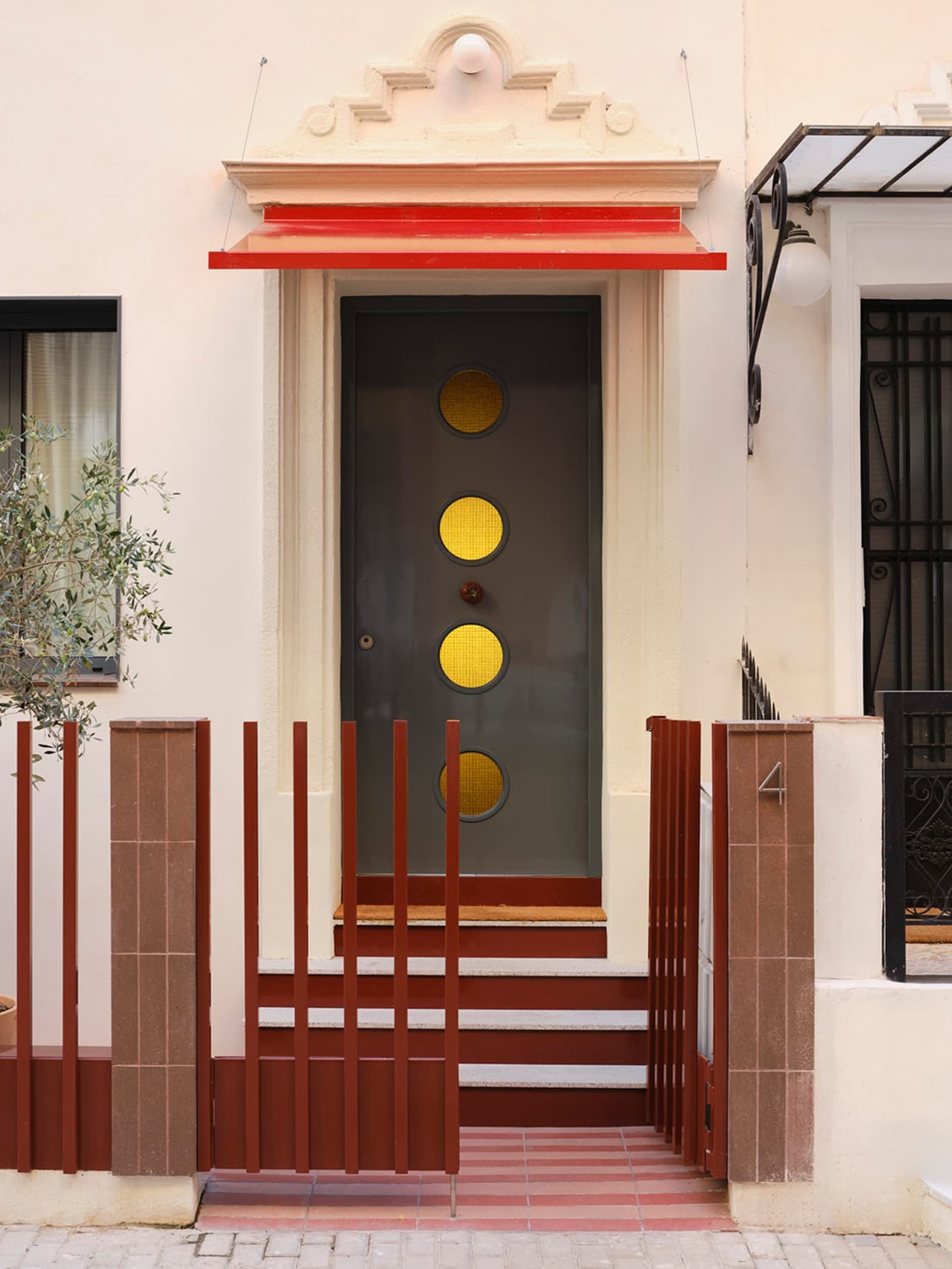 A traditional house with a white exterior, a red door, and a window, set in a natural outdoor setting with a potted plant in the foreground, lit by natural sunlight