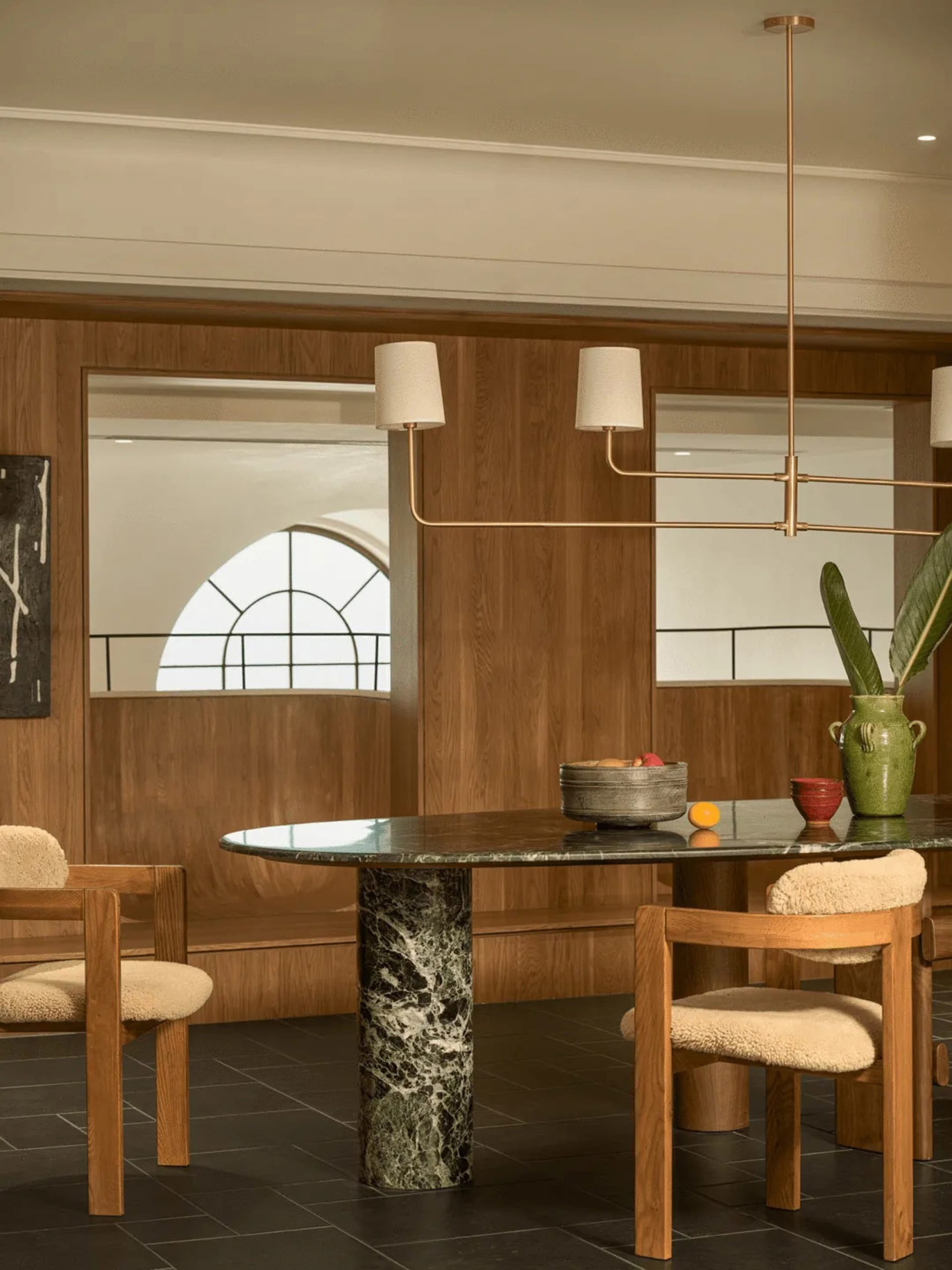 A dining room with a wooden table surrounded by chairs, set with a bowl, vase, and potted plant, creating a warm and inviting atmosphere with good lighting