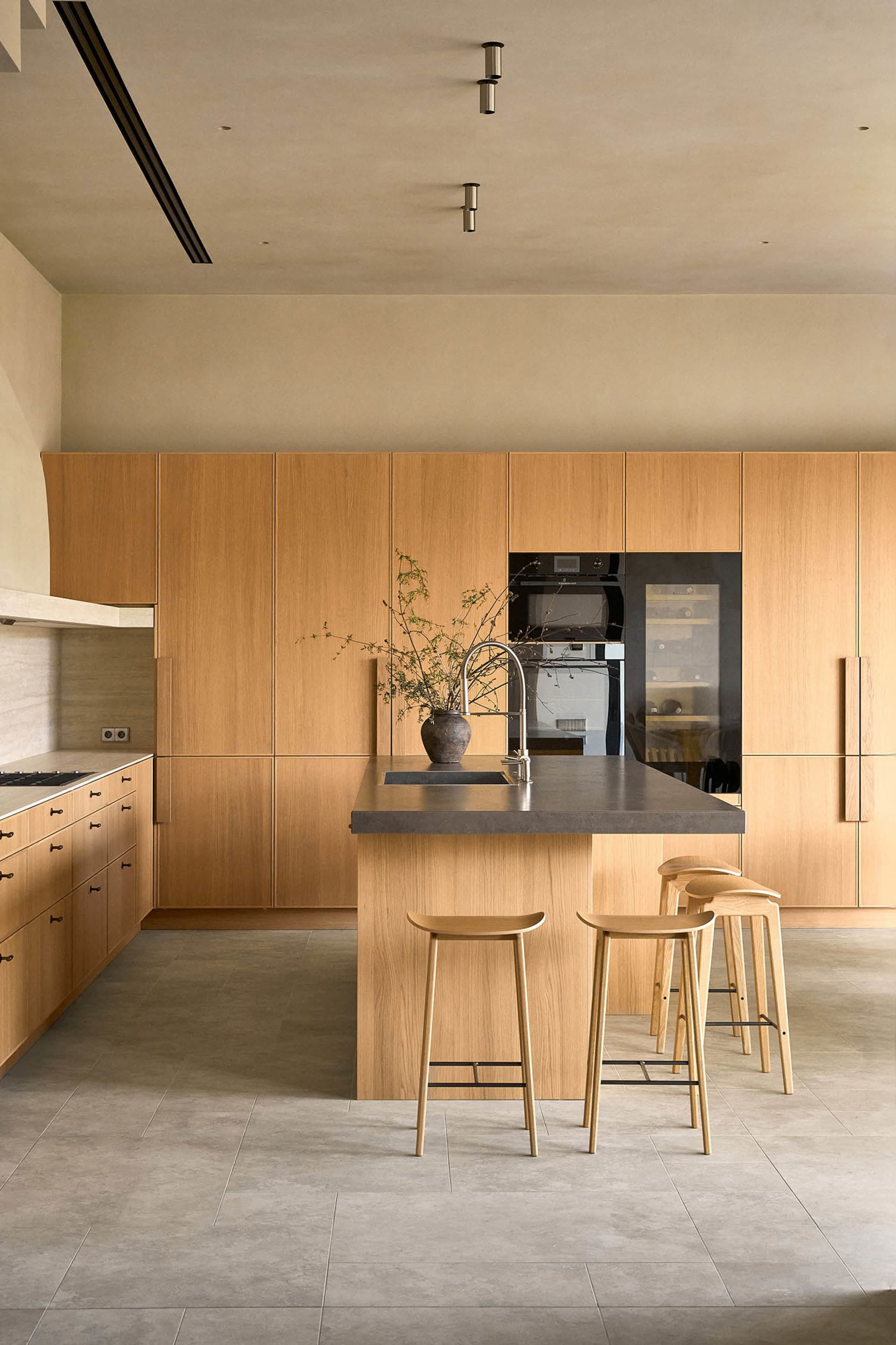 Warm and inviting kitchen with wooden cabinets and countertops, a center island with a sink, refrigerator, and oven, and three stools for seating
