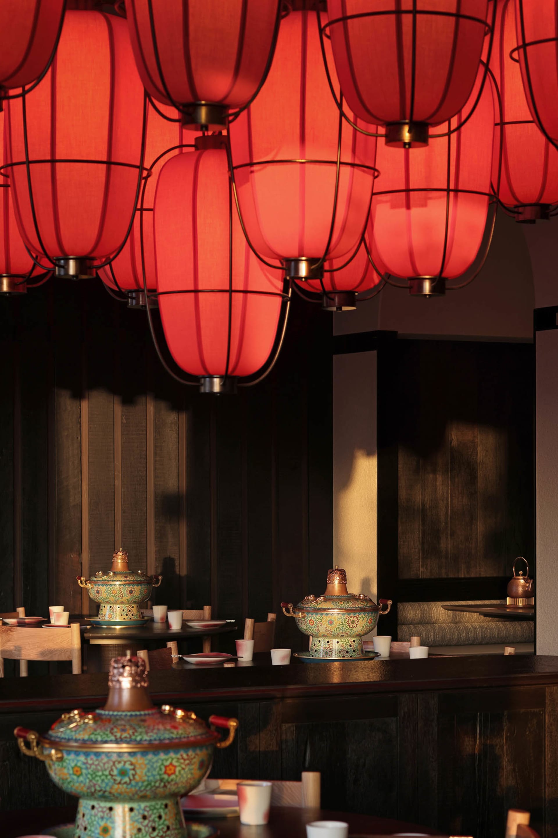 A modern restaurant dining area with a long wooden table and chairs, surrounded by ceramic bowls and cups, in a warm and inviting atmosphere