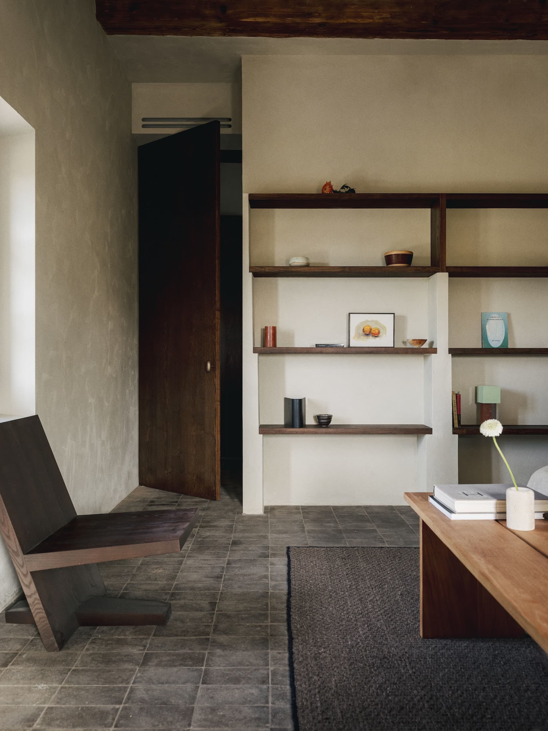A well-lit living room with a wooden floor, a bookshelf, a chair, a table, and a vase, creating a warm and inviting atmosphere