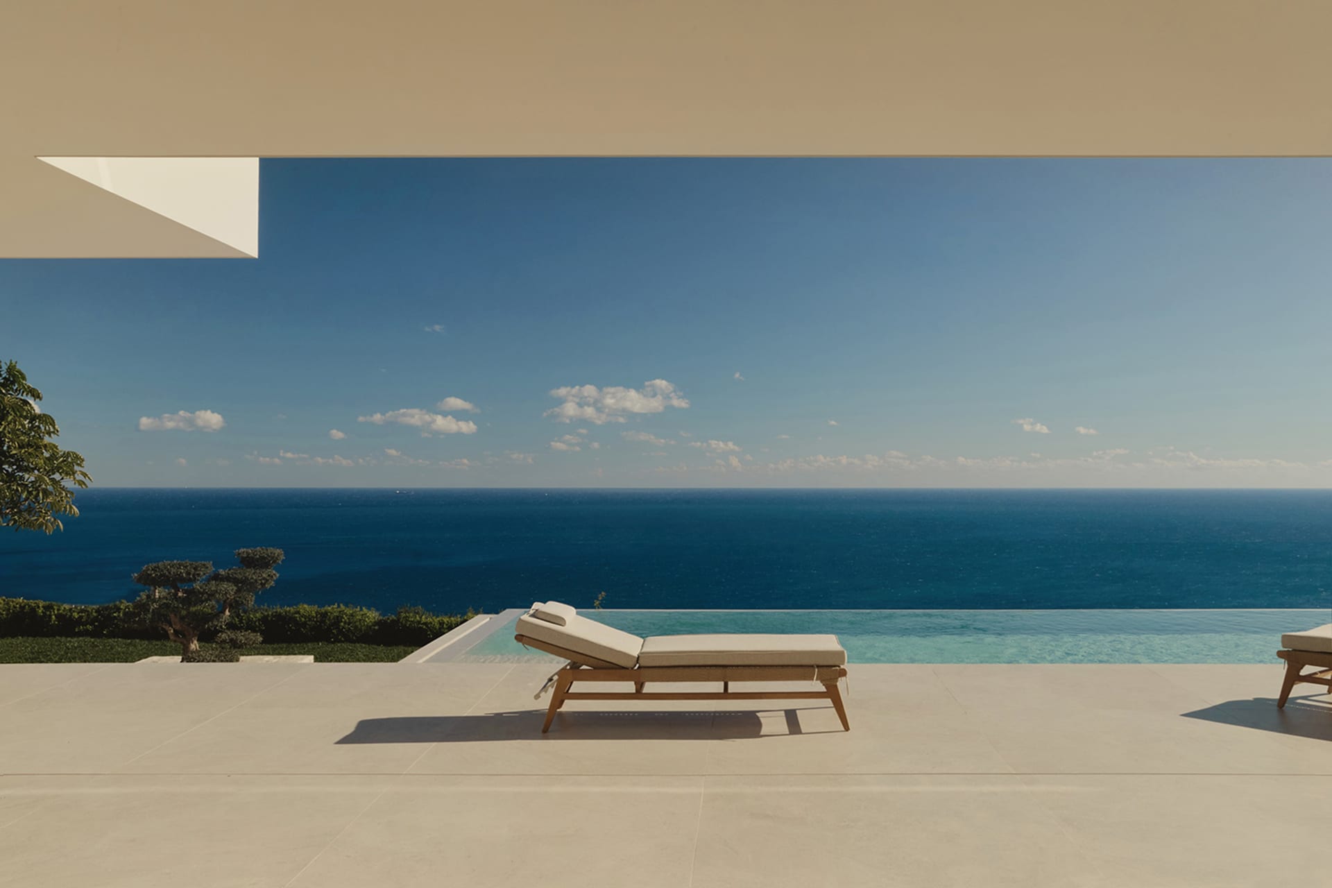 A serene outdoor patio with a white chair and couch on a white tile floor, overlooking a blue ocean with natural lighting and a clean modern aesthetic