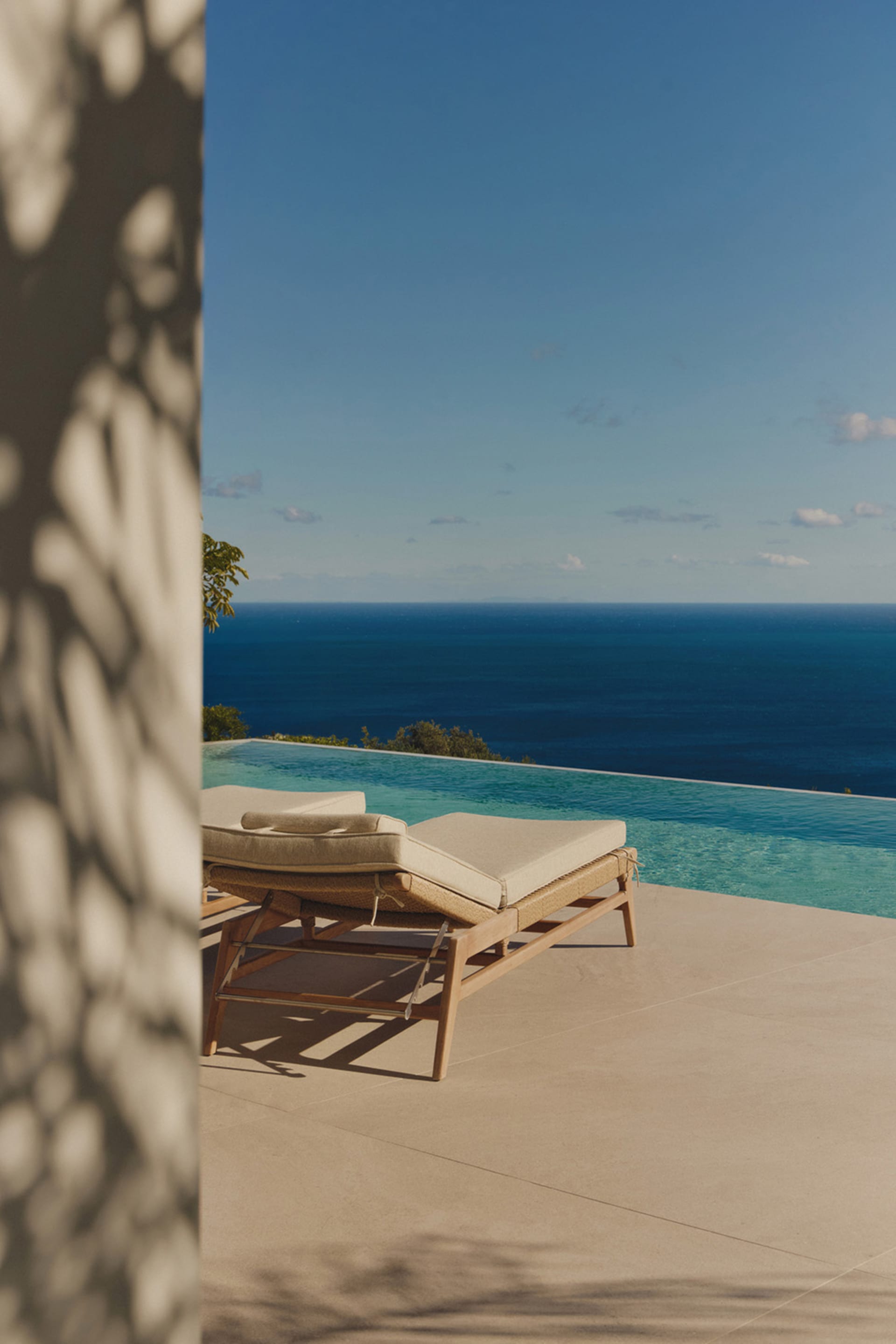A serene outdoor space with a wooden chair and couch on a concrete patio overlooking a blue ocean, perfect for relaxation and enjoying the view