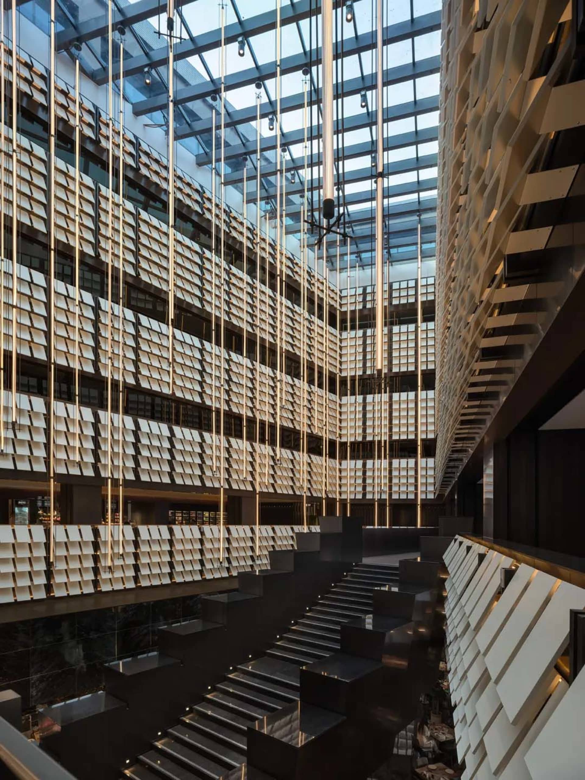 Large modern office building with a glass facade, open interior, and a metal staircase, lit by natural sunlight