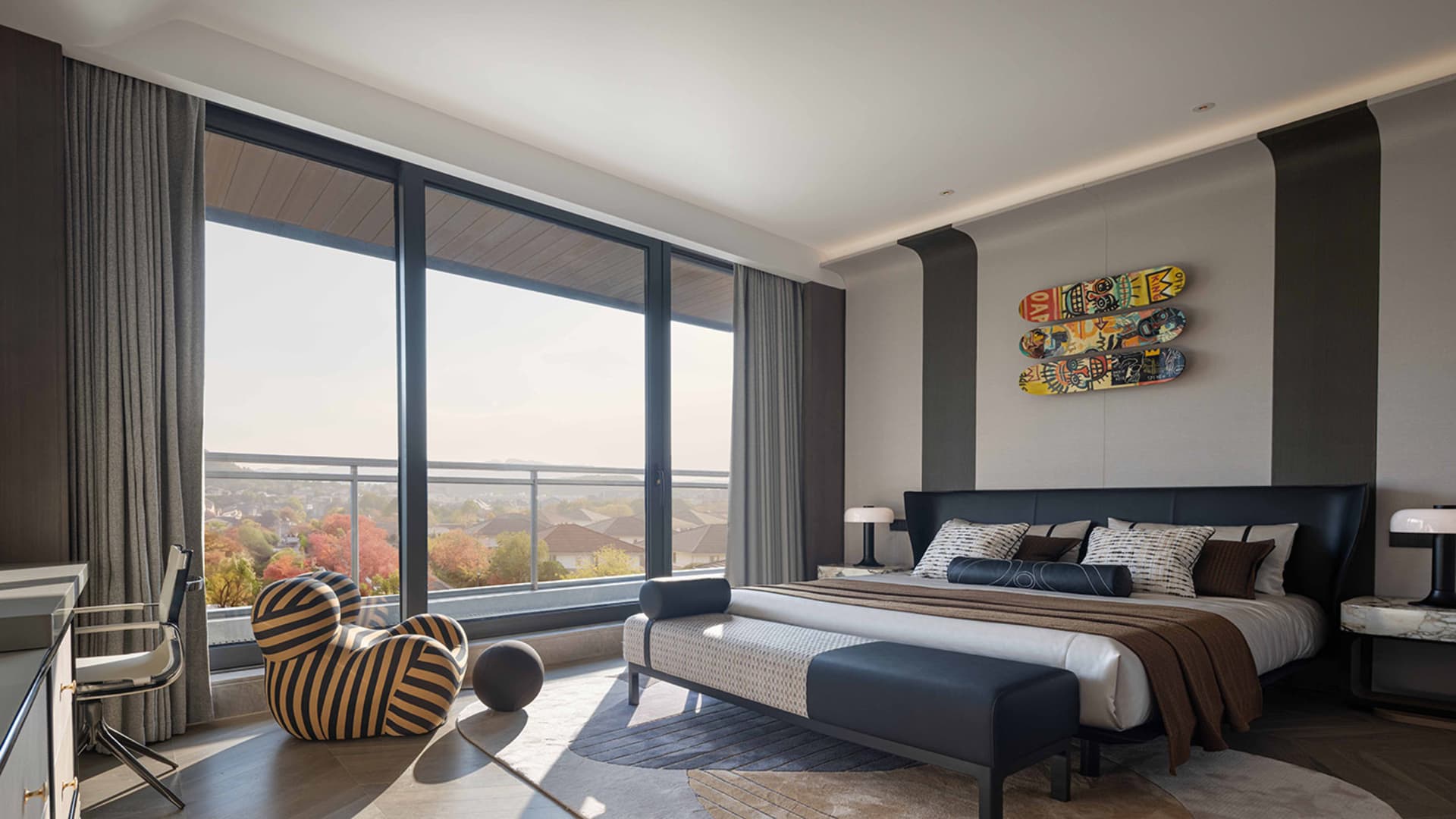 A modern bedroom with a bed, couch, and chair, featuring a large window and a predominantly white color scheme, with wood and leather furniture