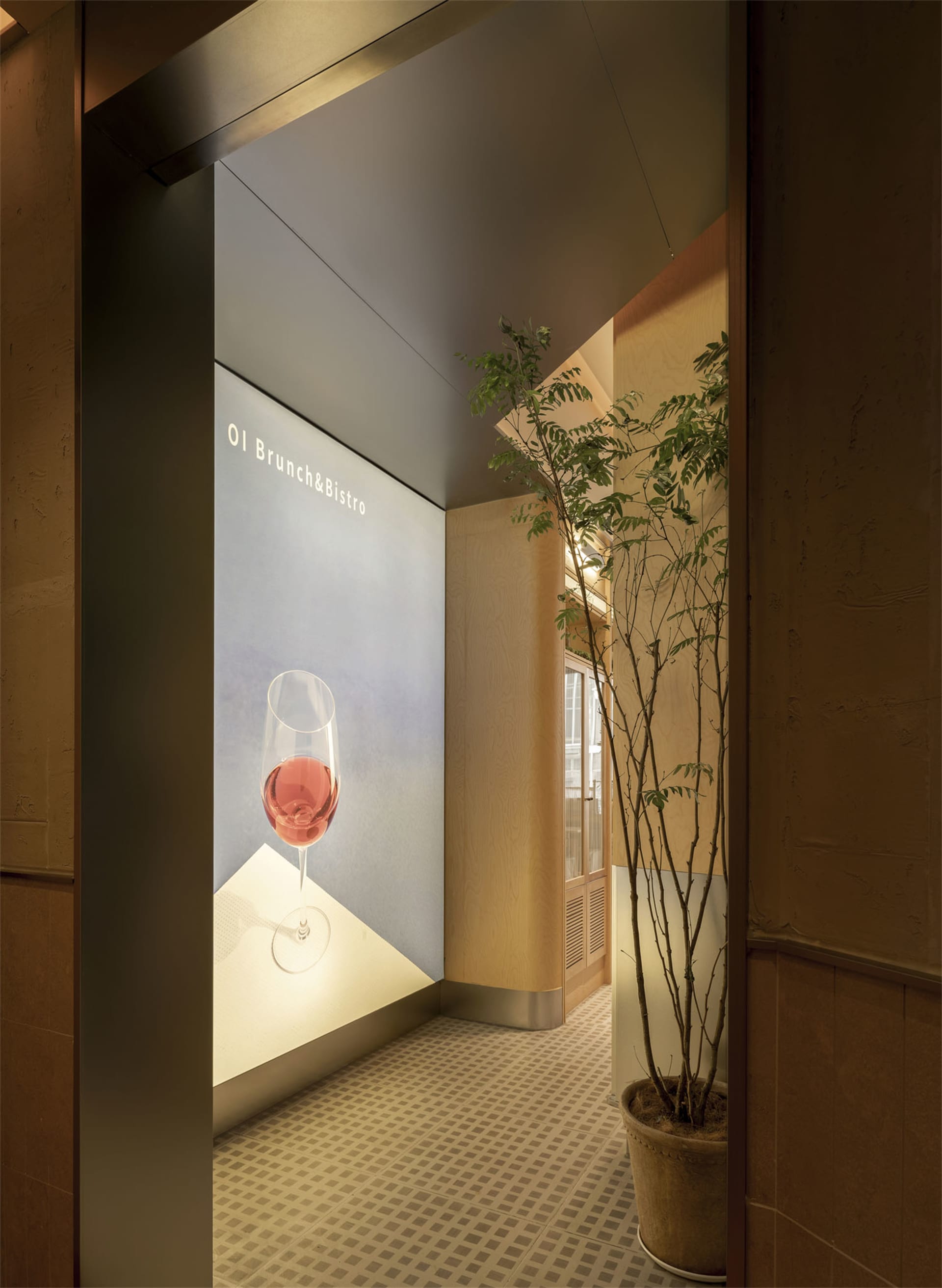 A wine glass sits on a table in a cozy wine bar with a potted plant in the corner and a dining table in the background, illuminated by warm lighting