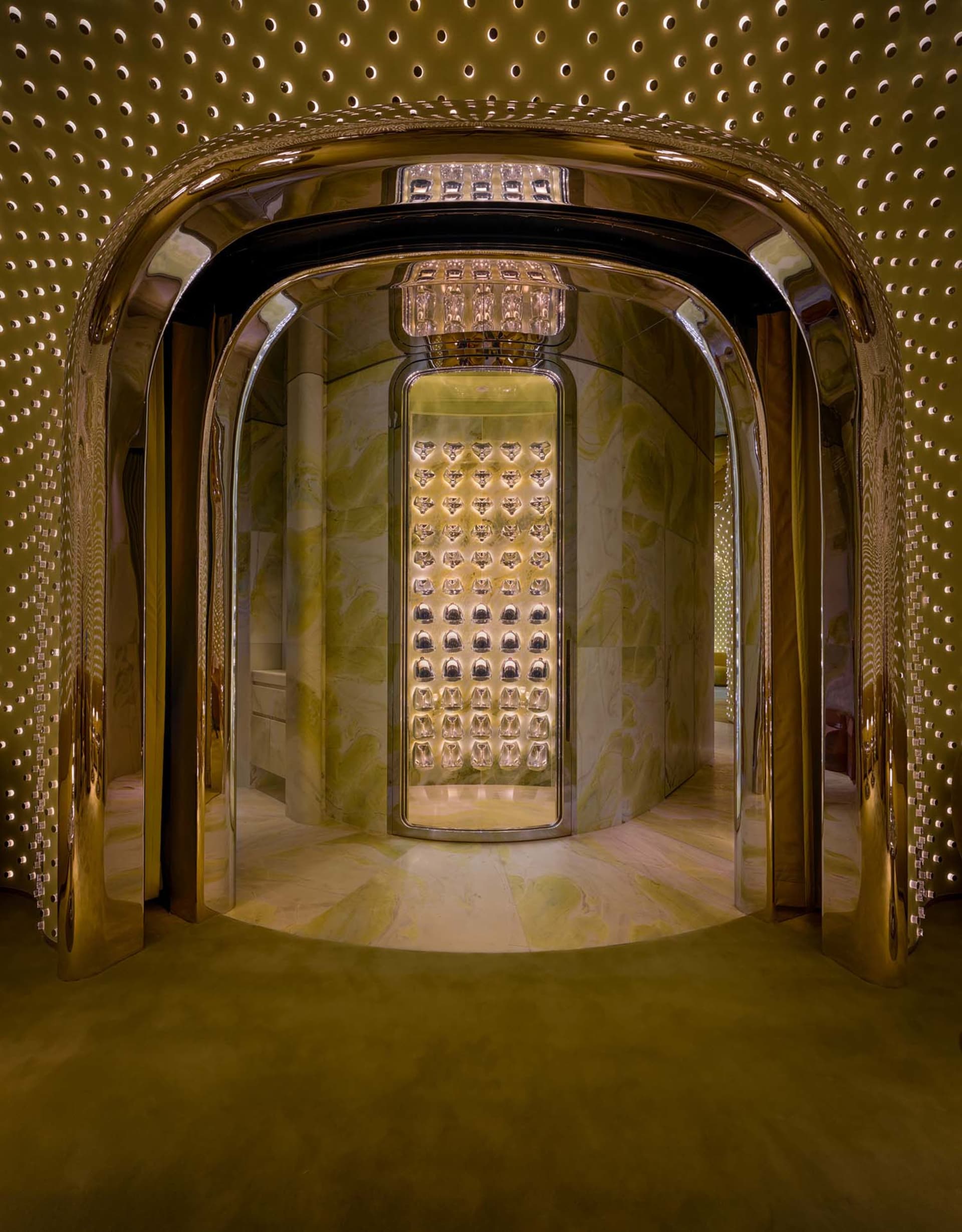A modern hallway with a gold-framed doorway, patterned wallpaper, and warm lighting