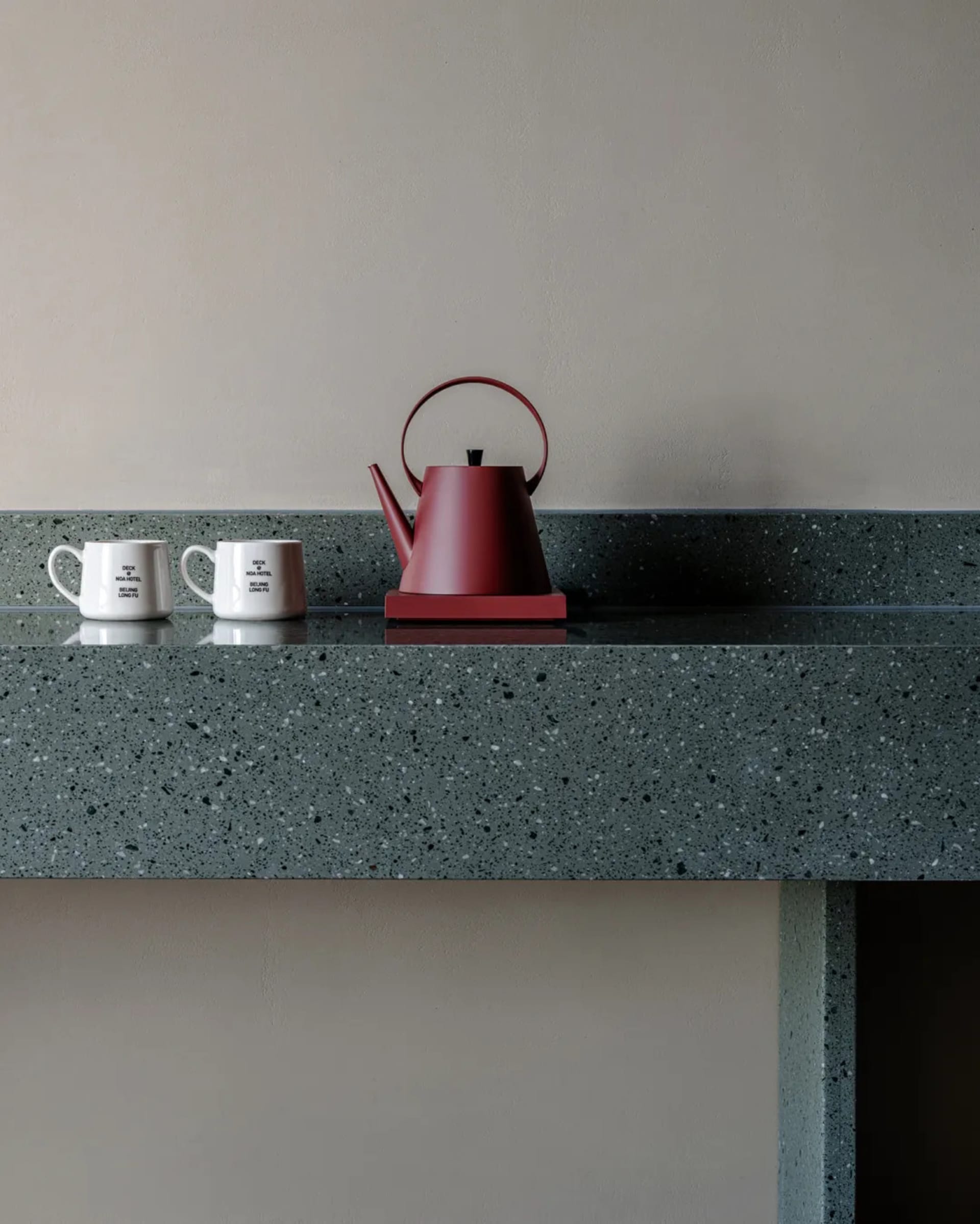 A kitchen counter with a red teapot and two white cups, set against a marble surface in a warm and inviting space