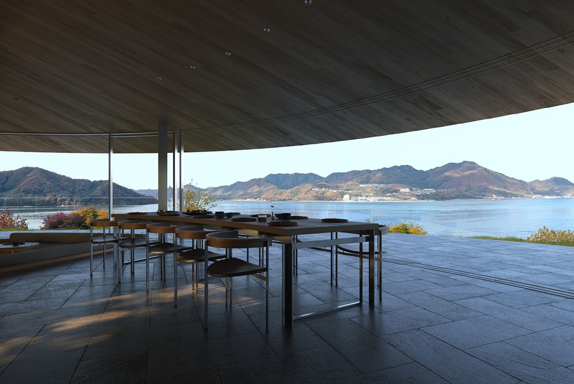 A well-lit dining room with a wooden table and chairs, surrounded by a large window with a view of the outdoors and a body of water
