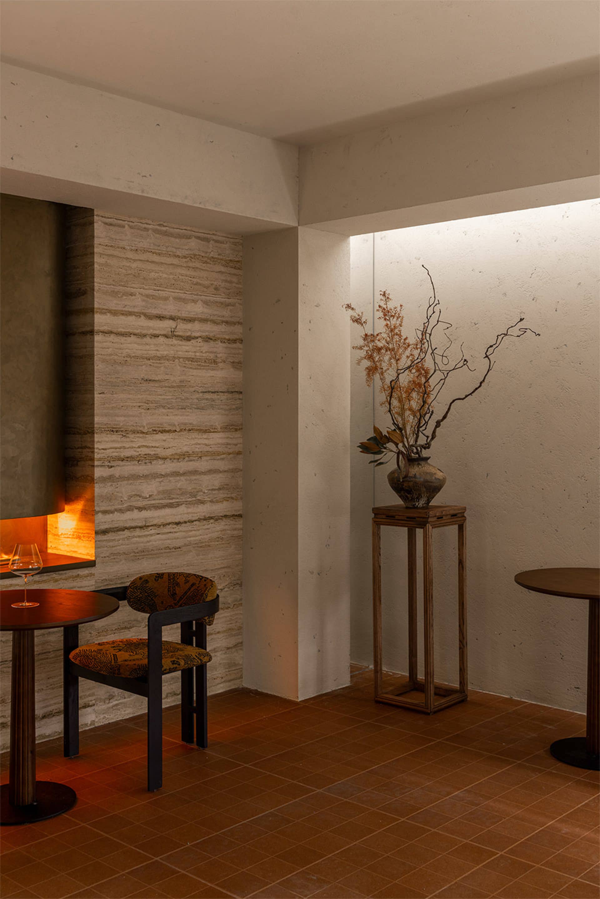 A warm and inviting dining area with a wooden table, chairs, and a vase with flowers, surrounded by stone walls and soft warm lighting