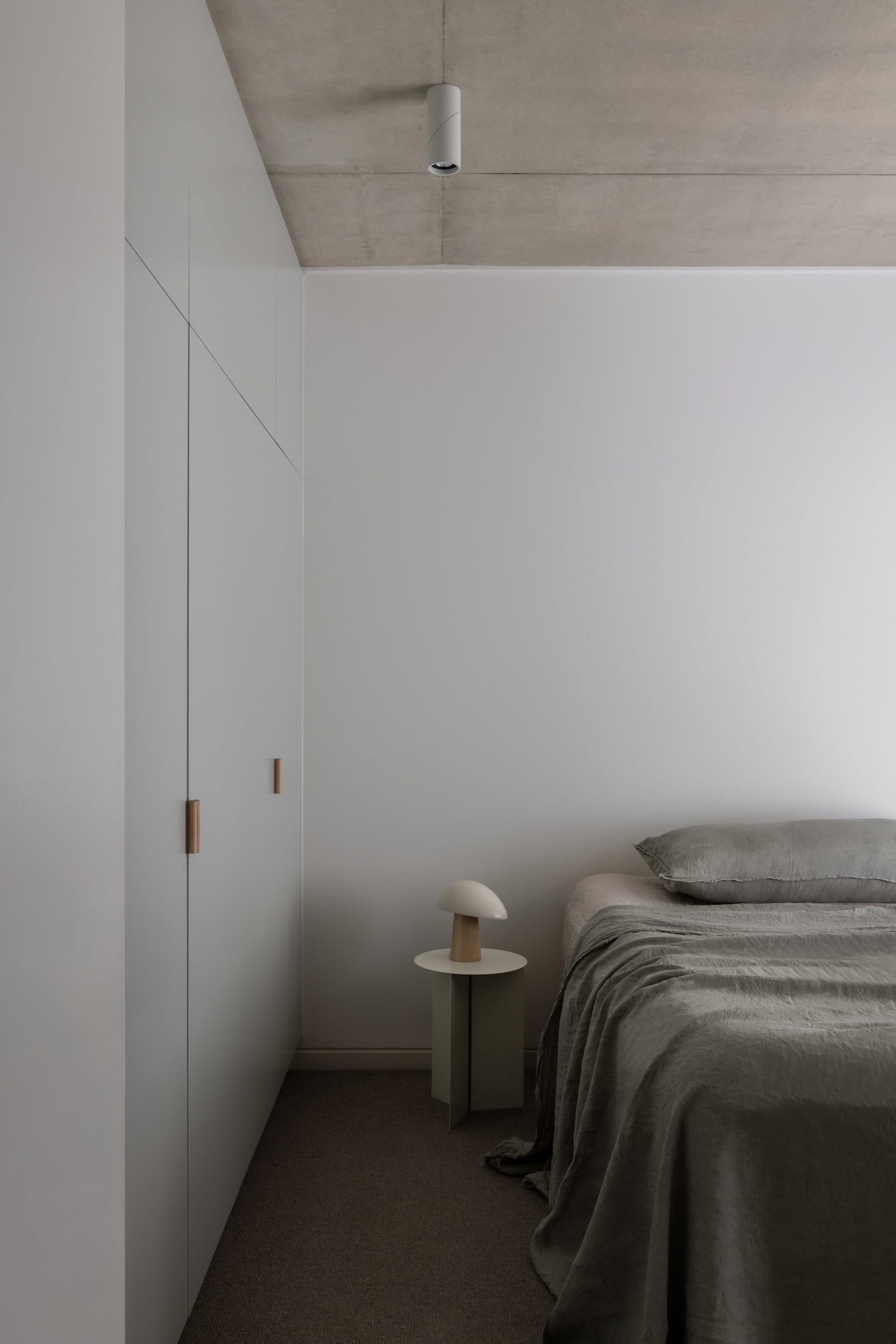 A dimly lit bedroom with a bed, a lamp, and a dresser, featuring wood and fabric materials