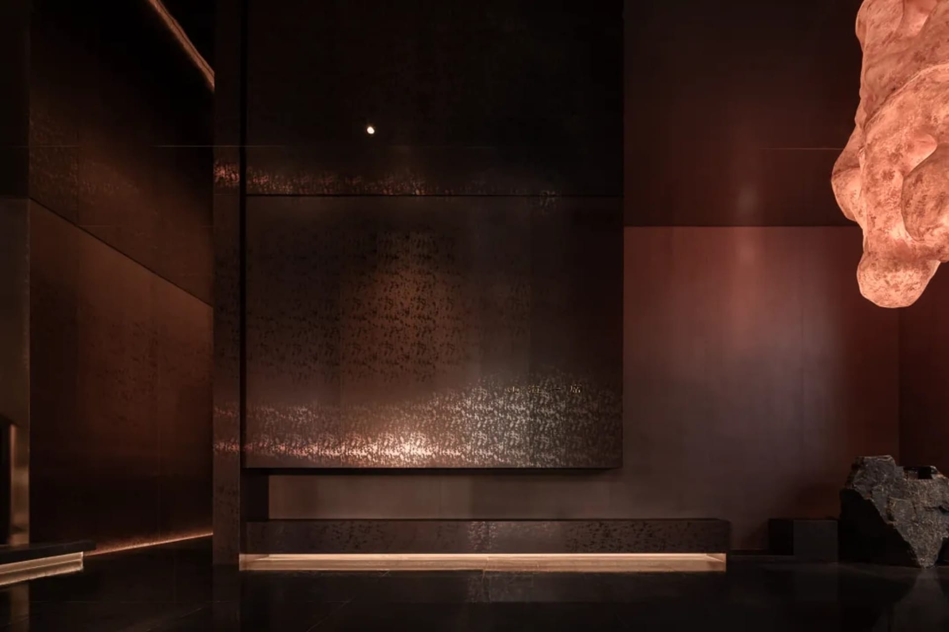 Dimly lit room with a brown wall, a bench, and a sense of depth from a low-angle perspective