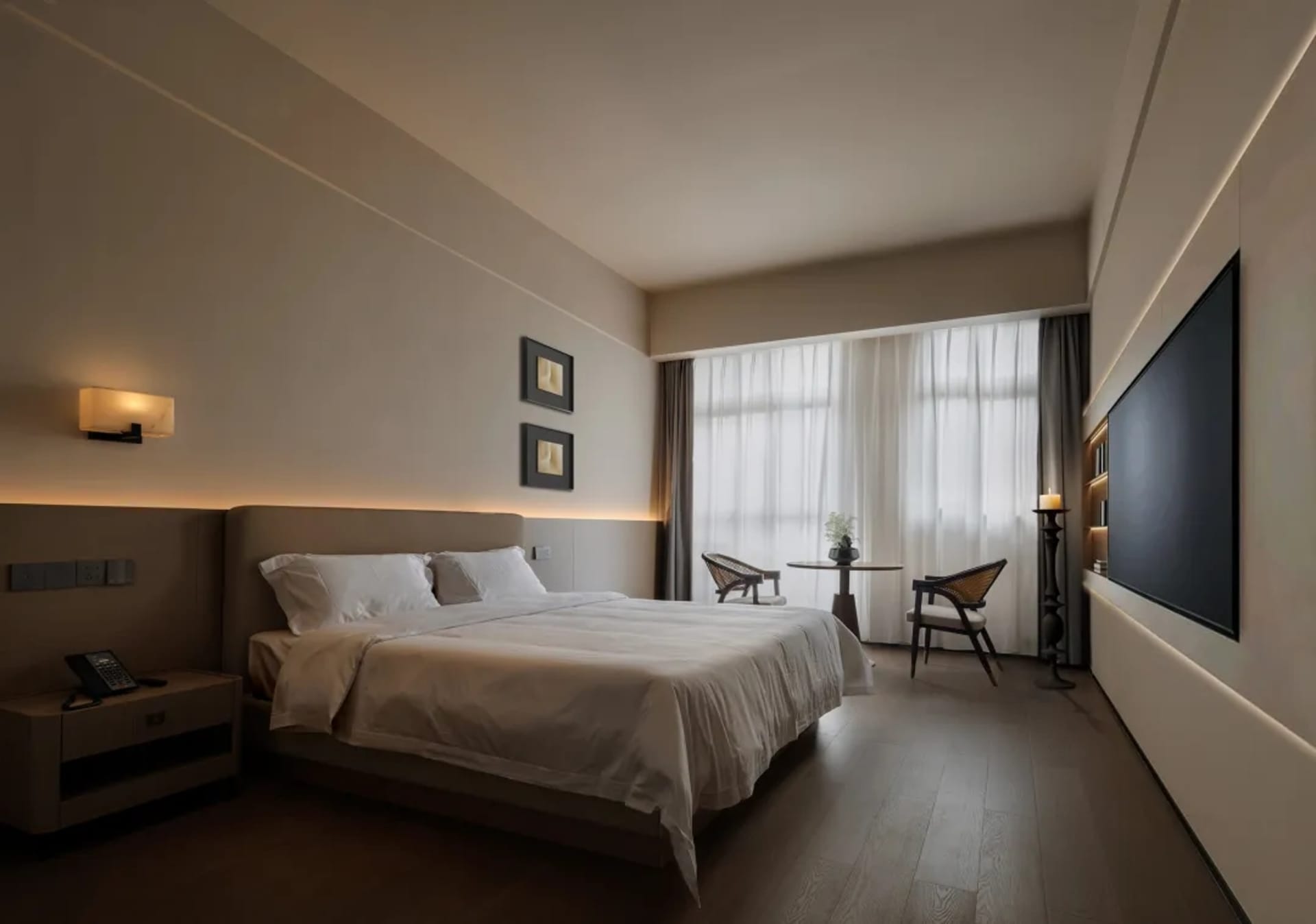 A calm and inviting bedroom with a bed, a wooden chair, and a table, well-lit and decorated with a white bed sheet