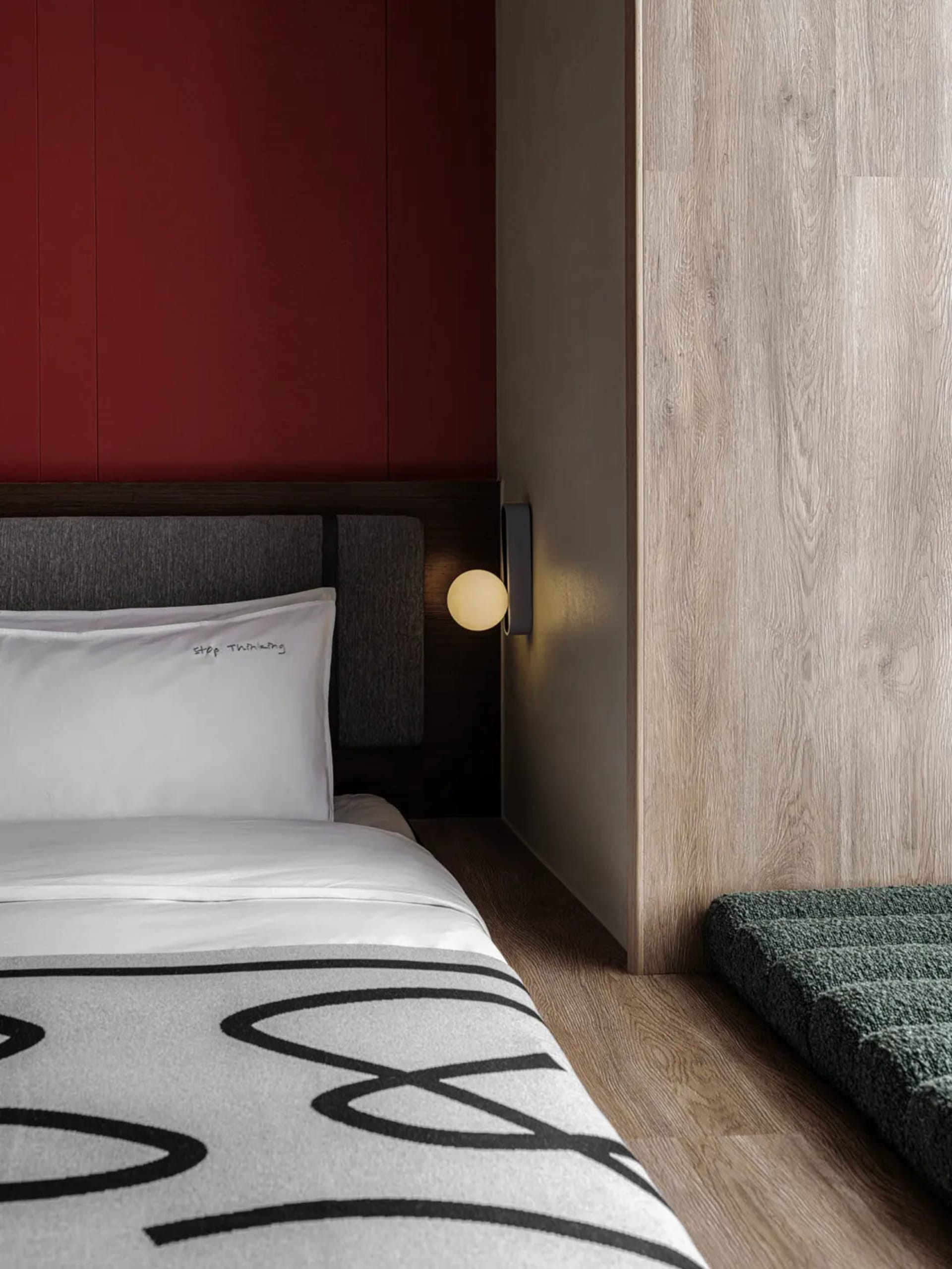 Cozy modern bedroom with a bed, nightstand, and red accent wall, well-lit with a white comforter and pillow