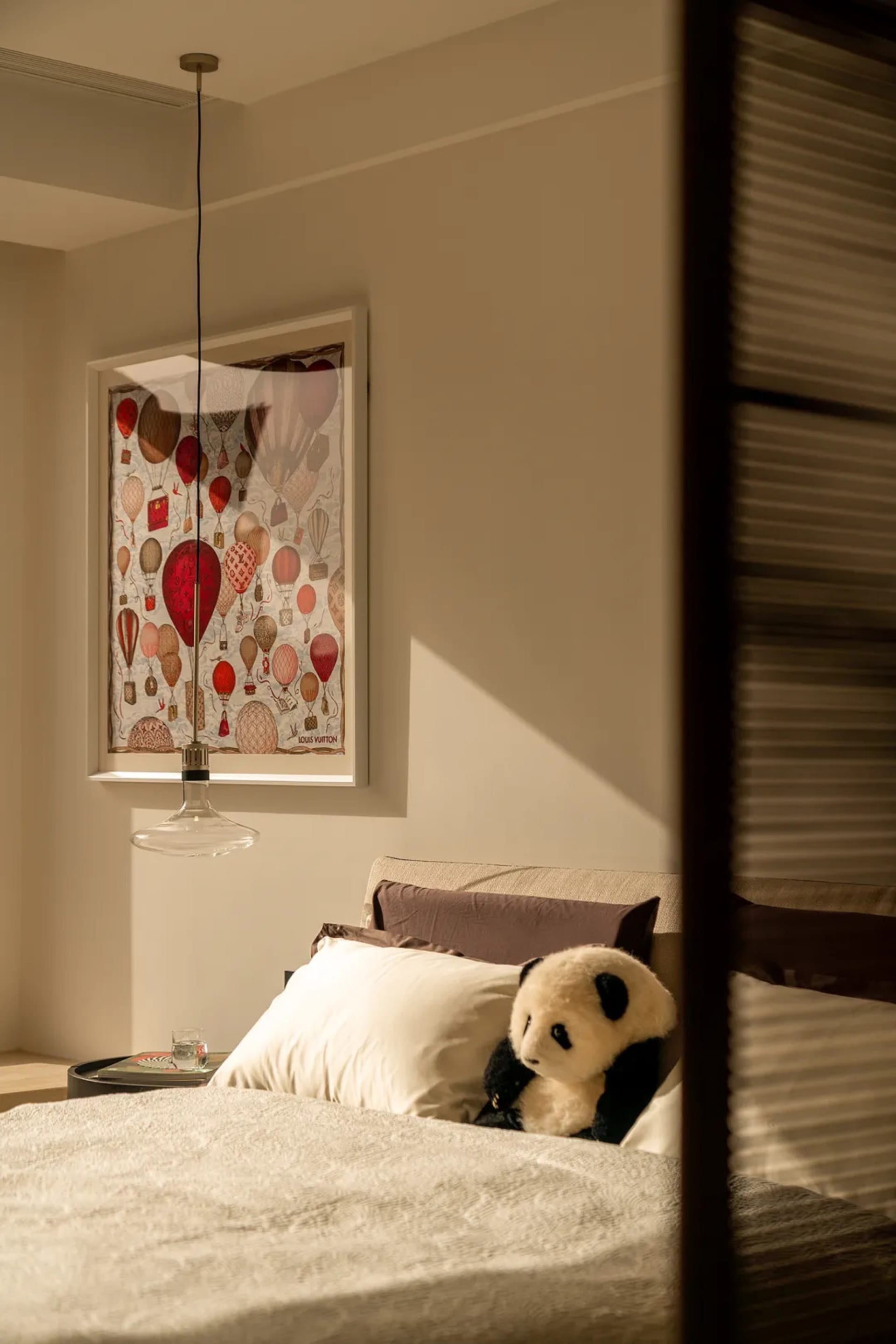 A dimly lit bedroom with a bed, a stuffed panda bear, and a picture on the wall