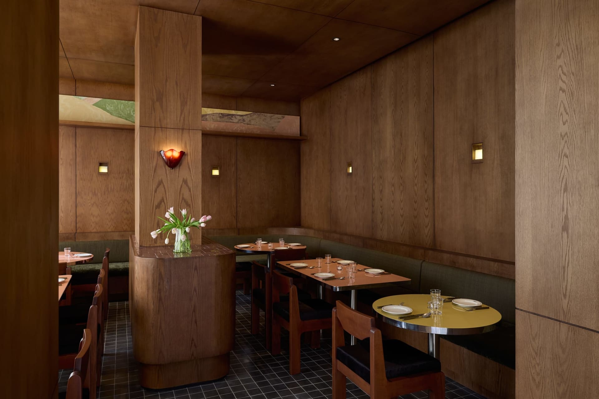 A warm and inviting restaurant interior with wooden tables, chairs, and decor, set with plates, wine glasses, and utensils, encouraging conversation and interaction among guests