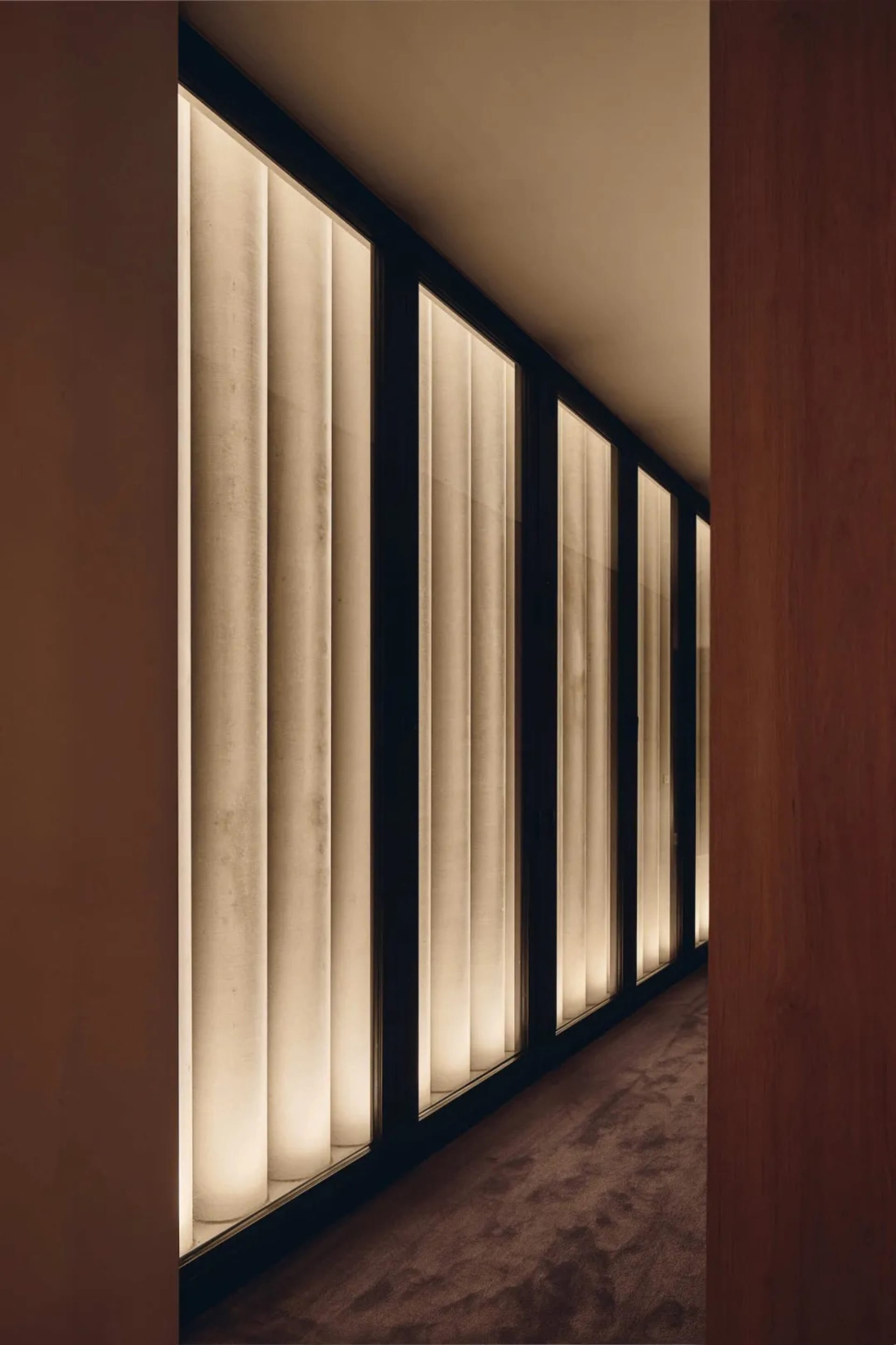 A modern residential hallway with glass windows, wood walls, and natural light, creating a bright and welcoming atmosphere