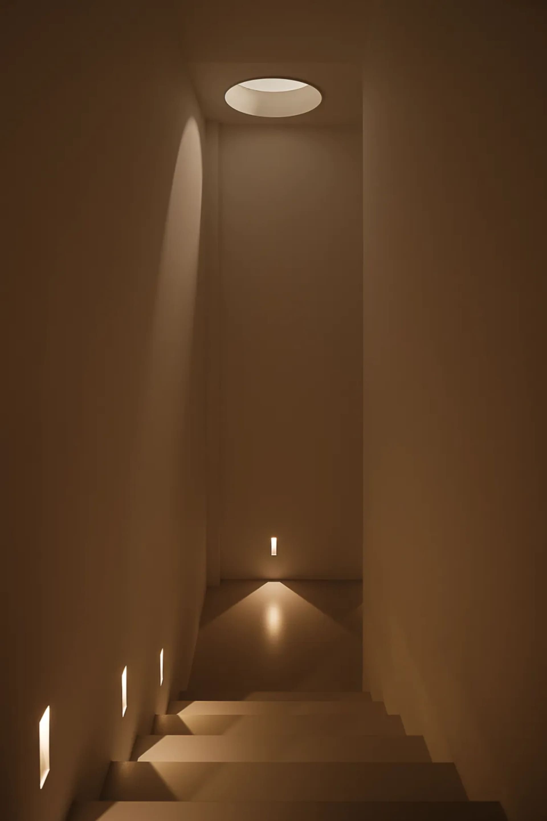 A bright and inviting hallway with a white concrete wall and a light shining down the center, illuminating the space