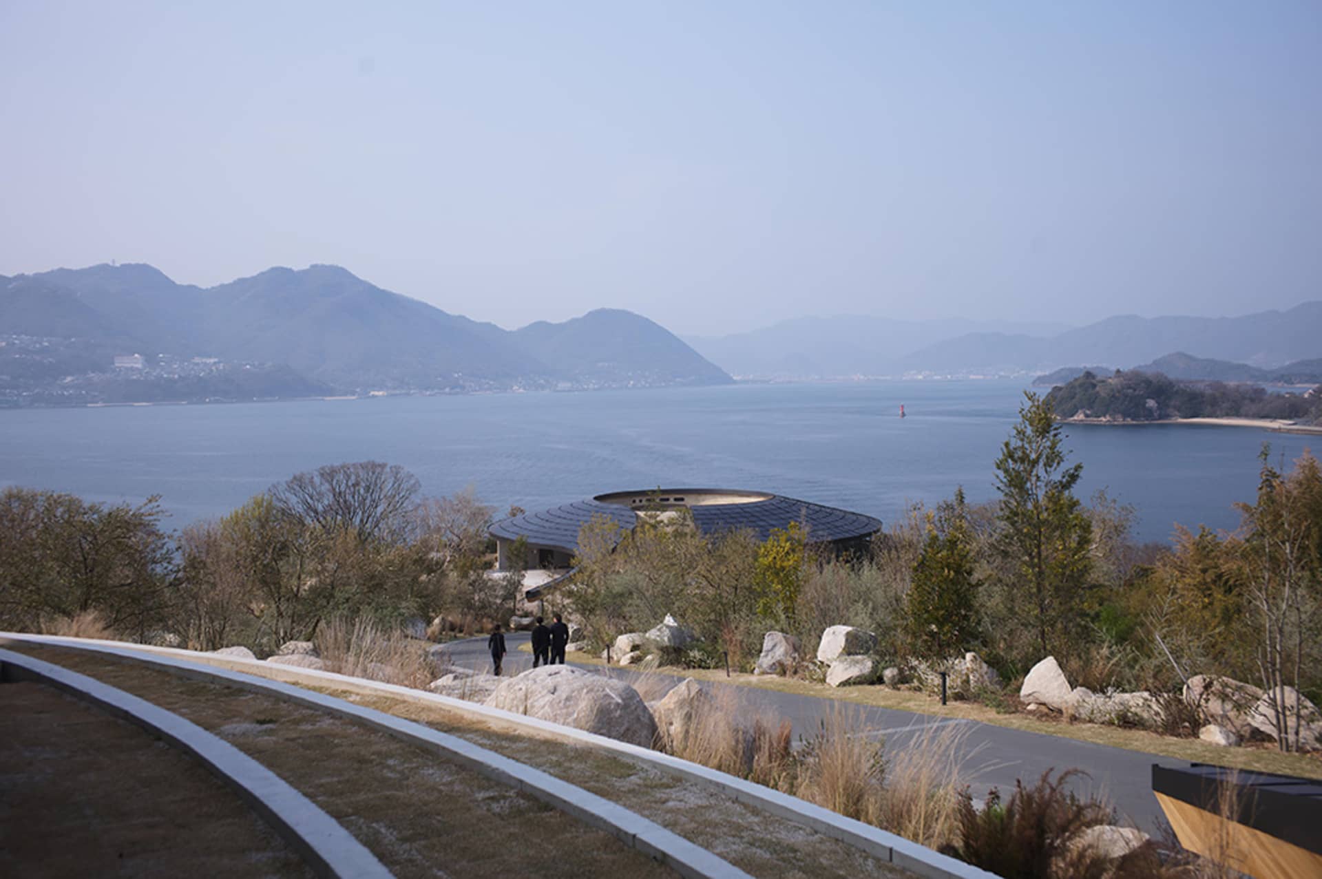 一座大型建築物靠近水體，中央有個圓形結構，人們走在周圍，融合建築和自然的元素