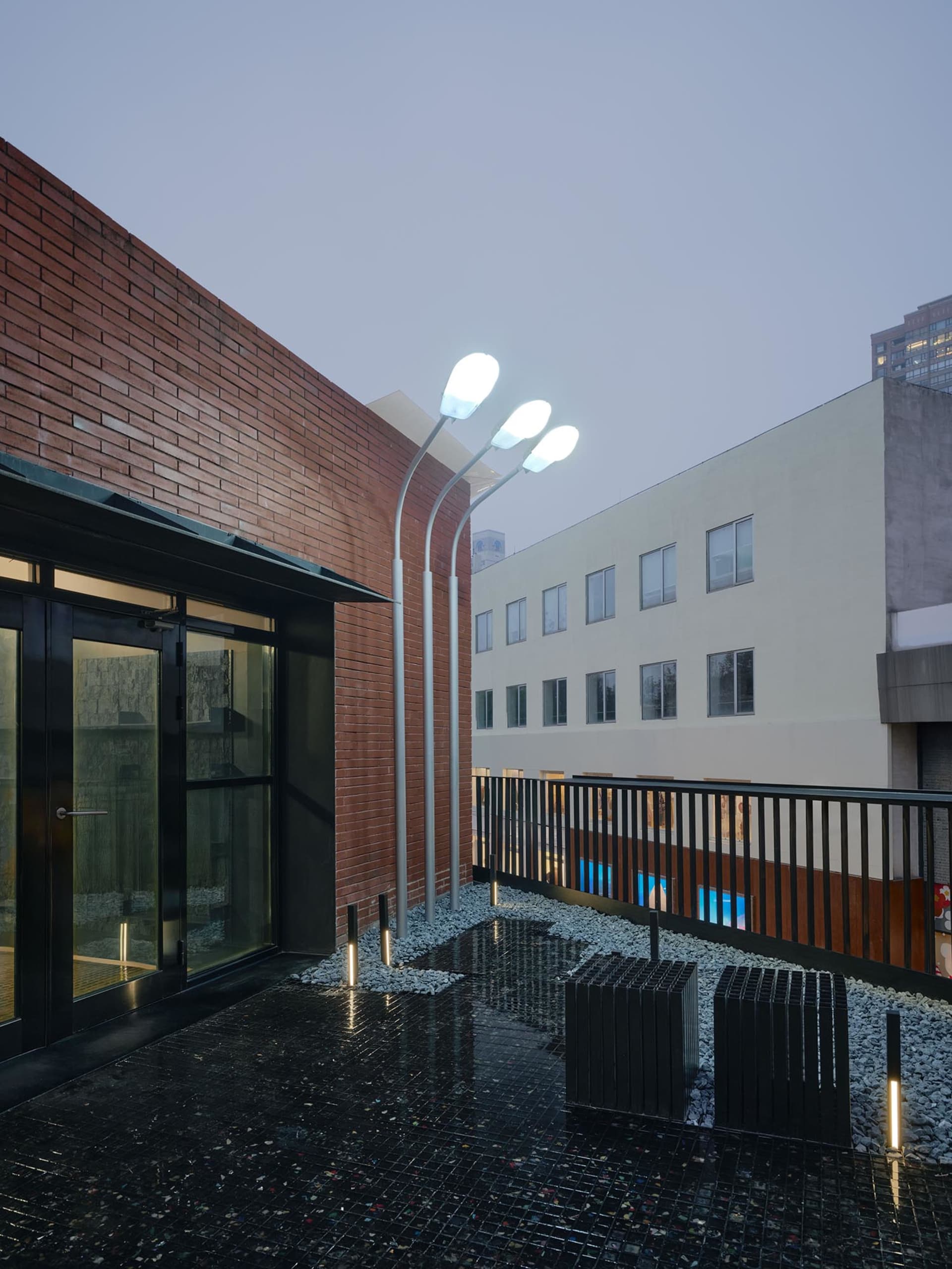Exterior photo of a modern building with a brick facade, a wooden balcony, and a stone patio, set in a dimly lit atmosphere