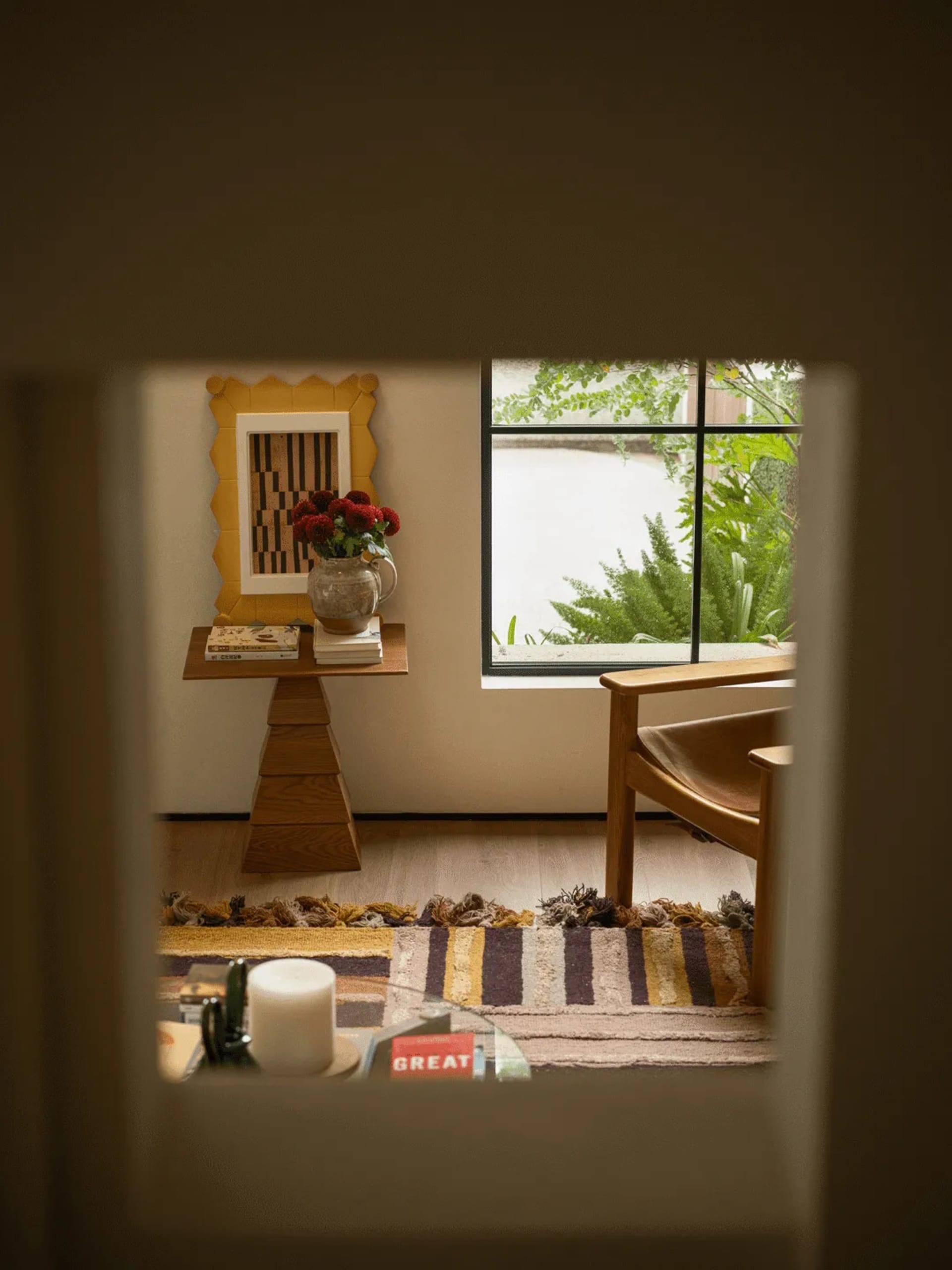 Cozy living room with a wooden floor, a couch, chair, and dining table, featuring natural light and a vase with flowers