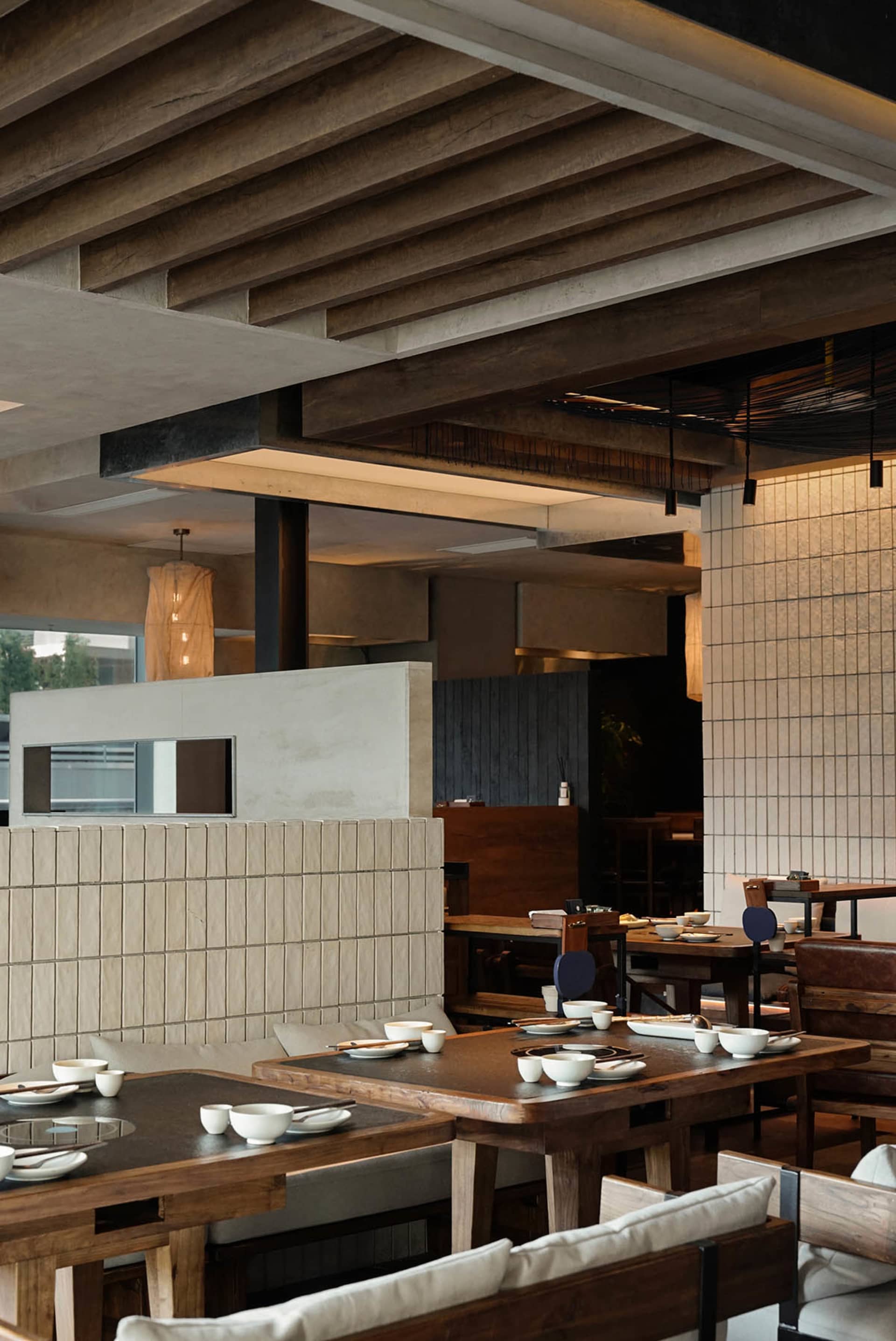 A modern restaurant interior with wood paneling, natural lighting, and a variety of materials, featuring tables, chairs, and dining area