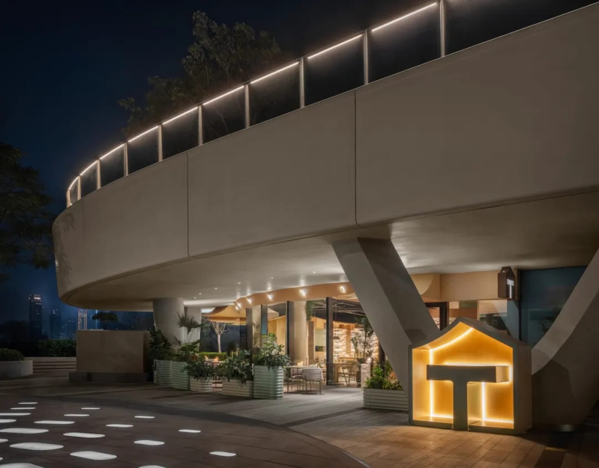 A modern building with a large patio area surrounded by potted plants and a dining table, creating an inviting and comfortable atmosphere