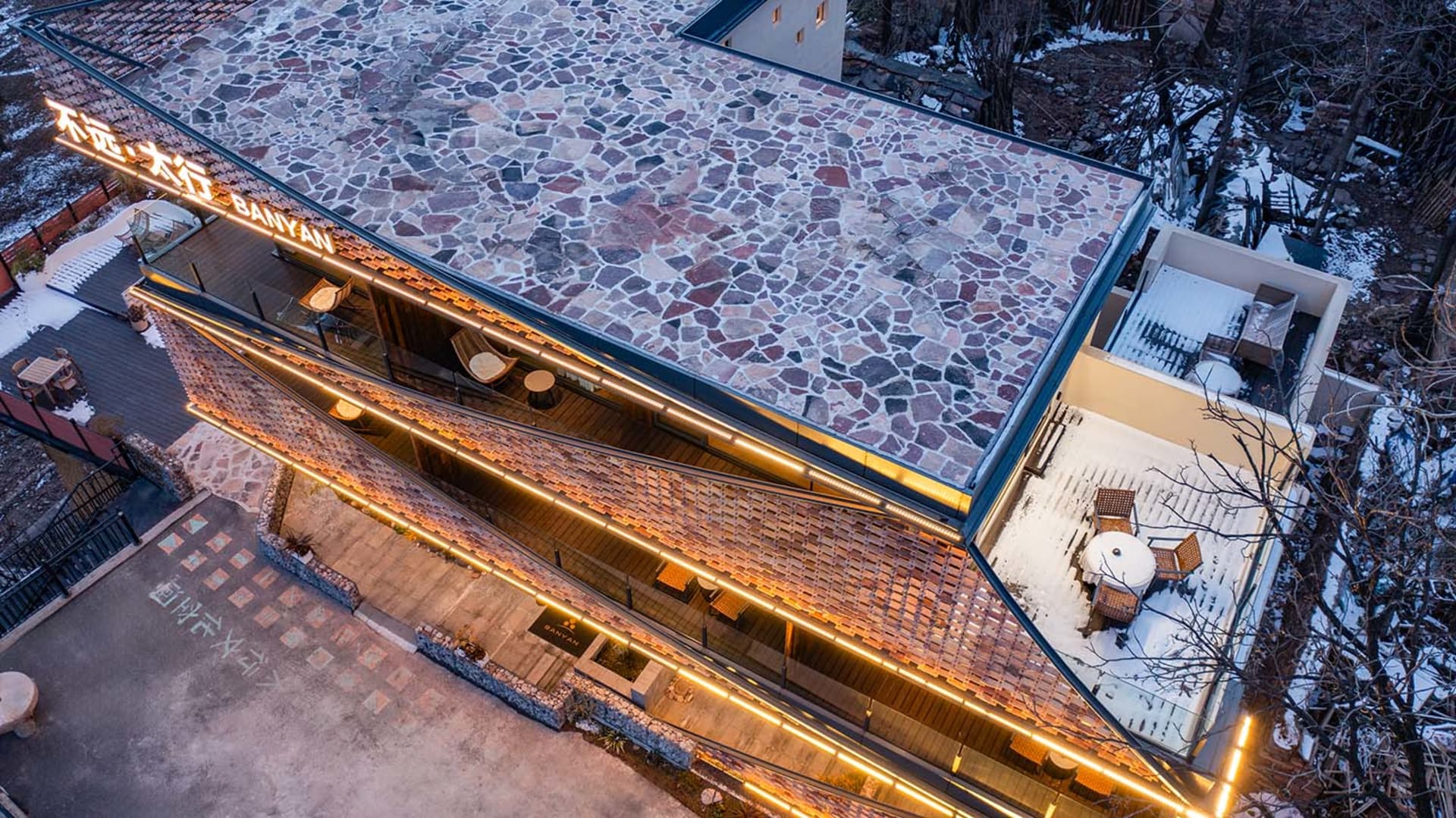 A stone-roofed restaurant with a rustic and natural appearance, featuring a blend of stone and wood elements, brick details, and outdoor seating with dining tables and chairs
