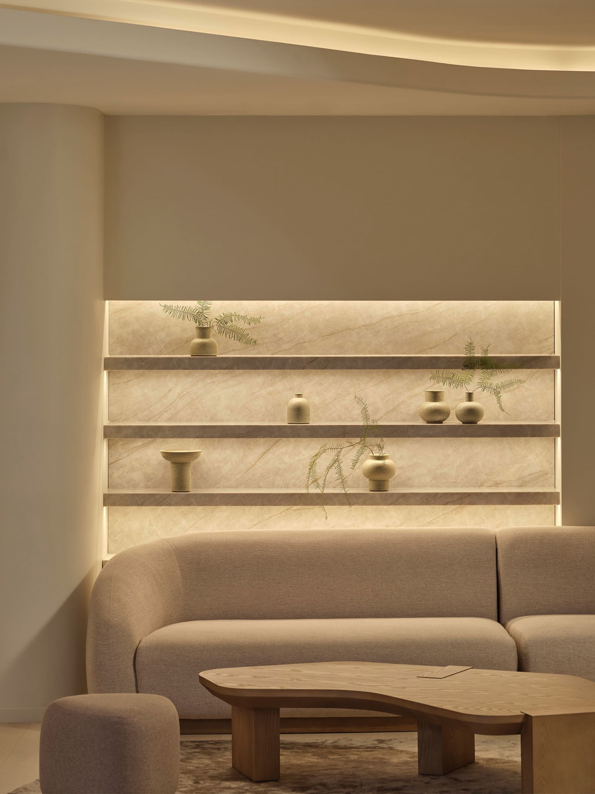 Cozy living space with beige walls, a couch, coffee table, and shelf, well-lit for a comfortable atmosphere