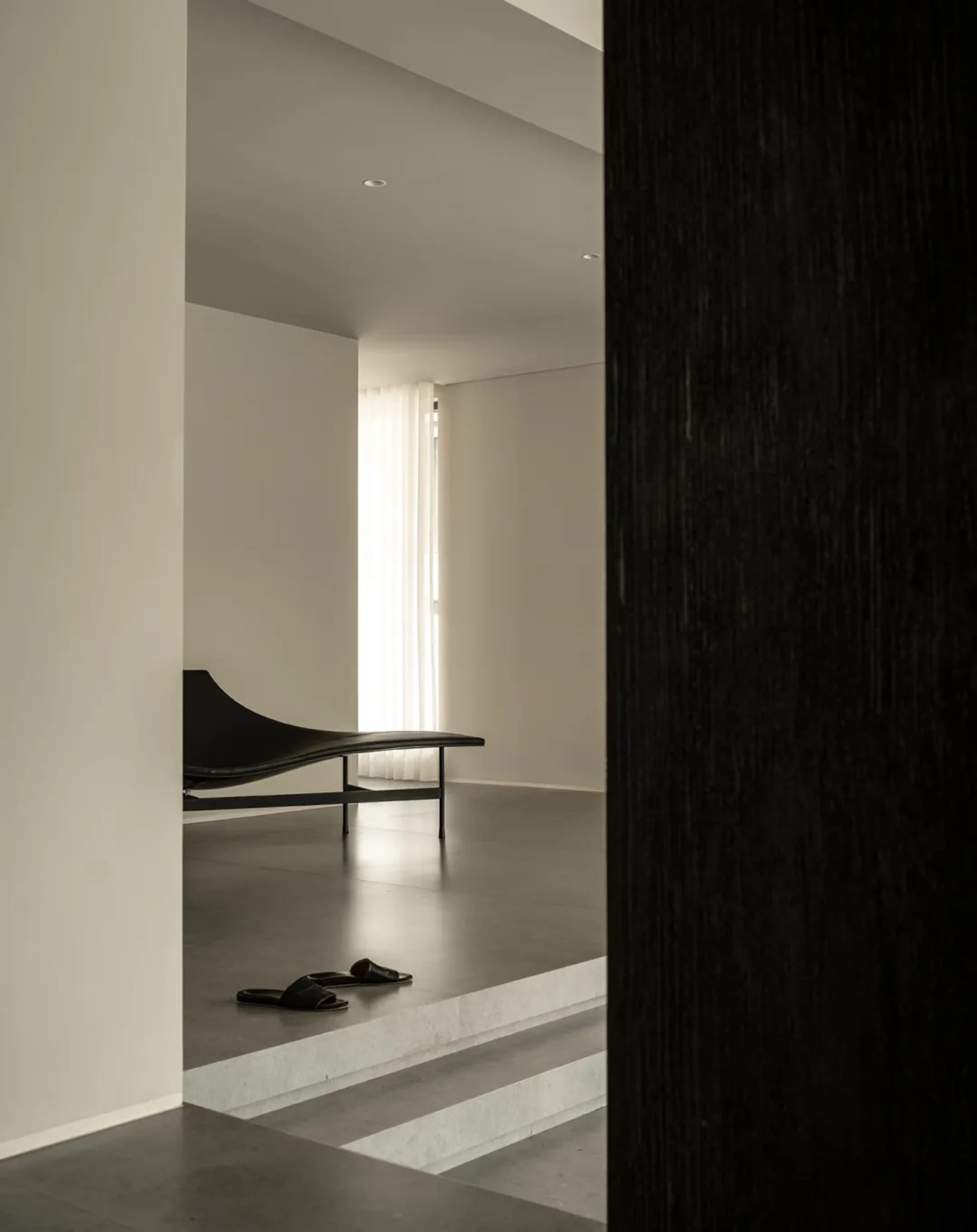 A dimly lit room with a black couch and bench in a minimalist and modern space with a black and white color scheme