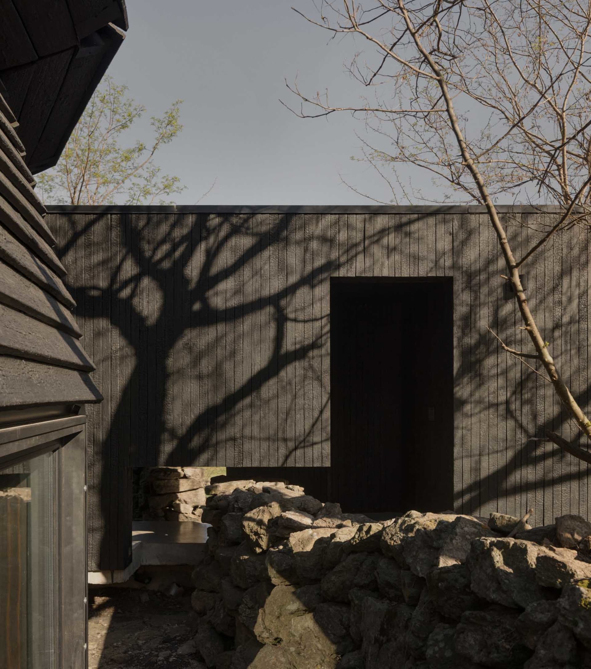 A modern house with a wooden exterior, large window, and door, surrounded by trees, in a calm and serene natural setting