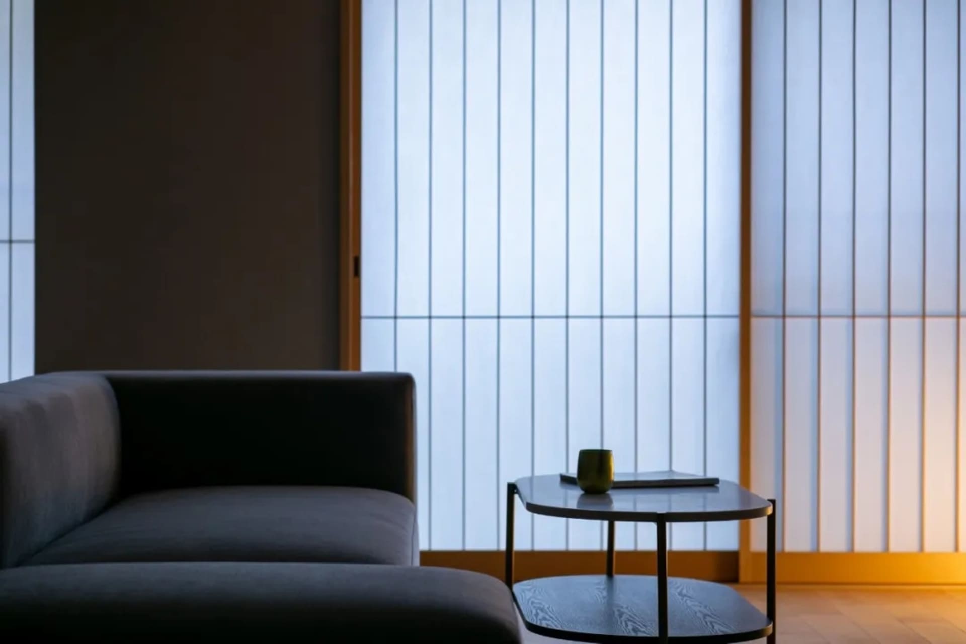 Cozy modern living room with a gray couch, a black table, and dim lighting, decorated with a cup and a vase, featuring wood and metal materials
