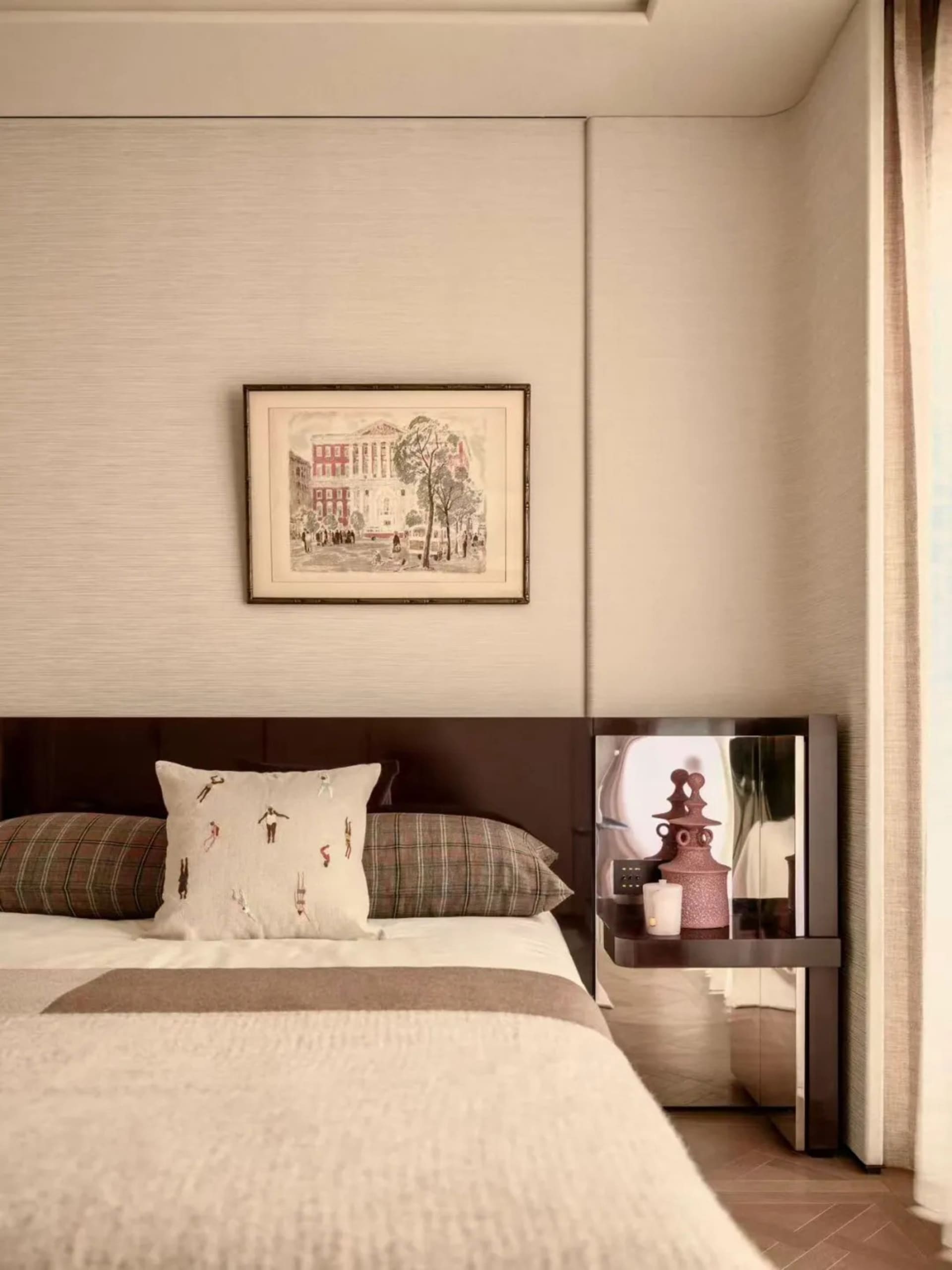Cozy bedroom with a bed covered in a white blanket, a wooden headboard, and a picture frame on the wall, with a table and lamp nearby