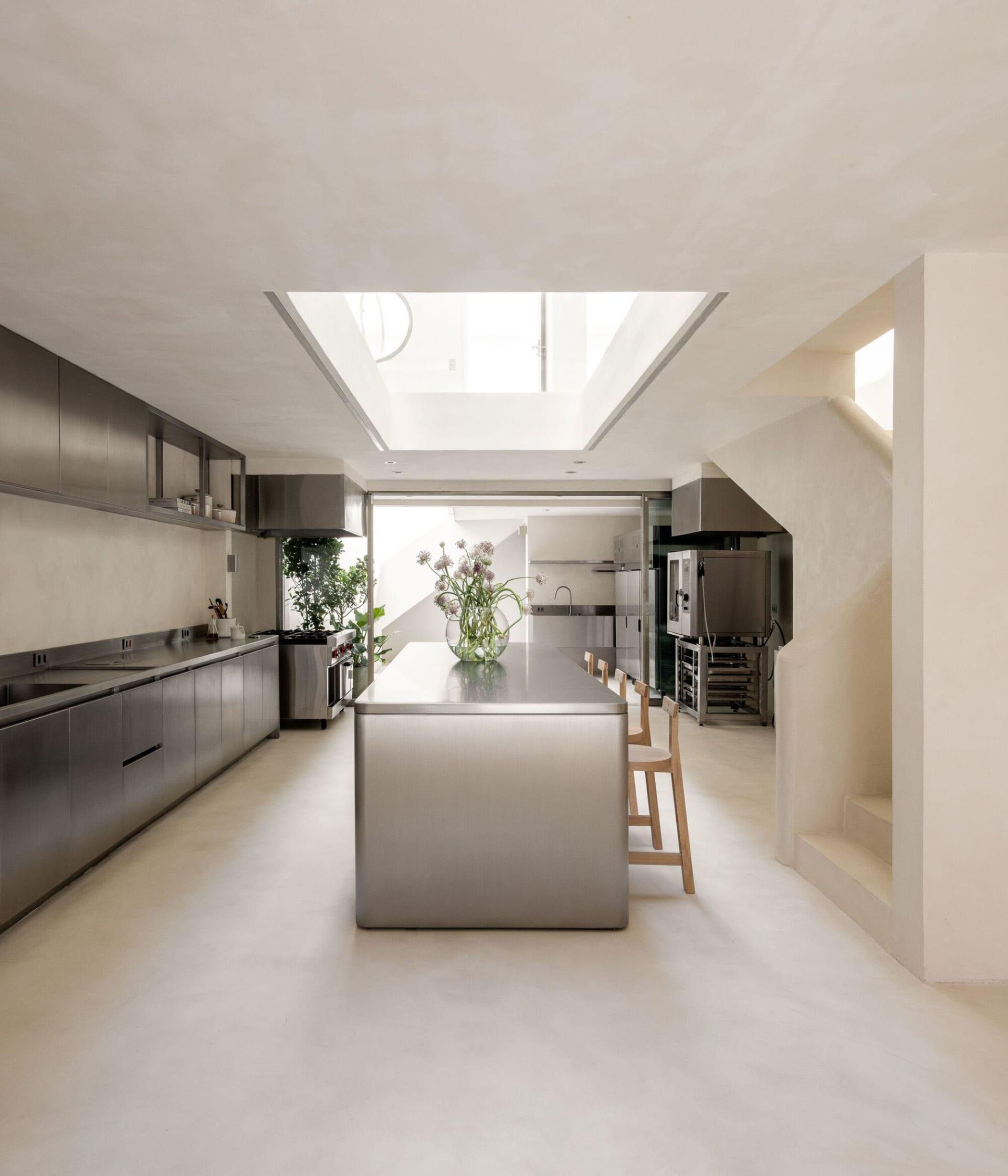 Modern kitchen and dining space with a large island, dining table, potted plants, and vases, featuring a clean and functional design