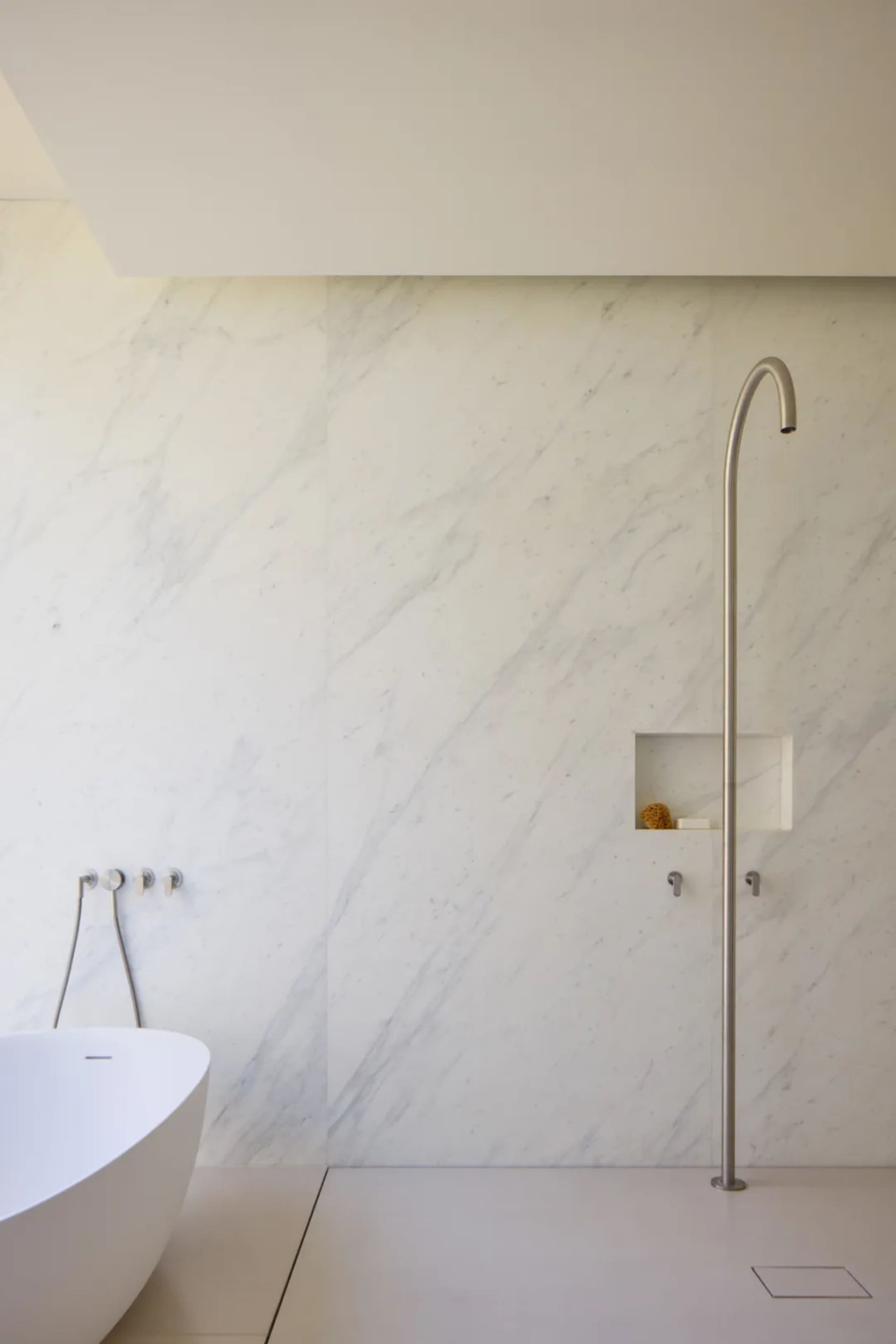 Bathroom with a white bathtub, marble walls, and a metal shower rod, set against a clean and well-maintained backdrop