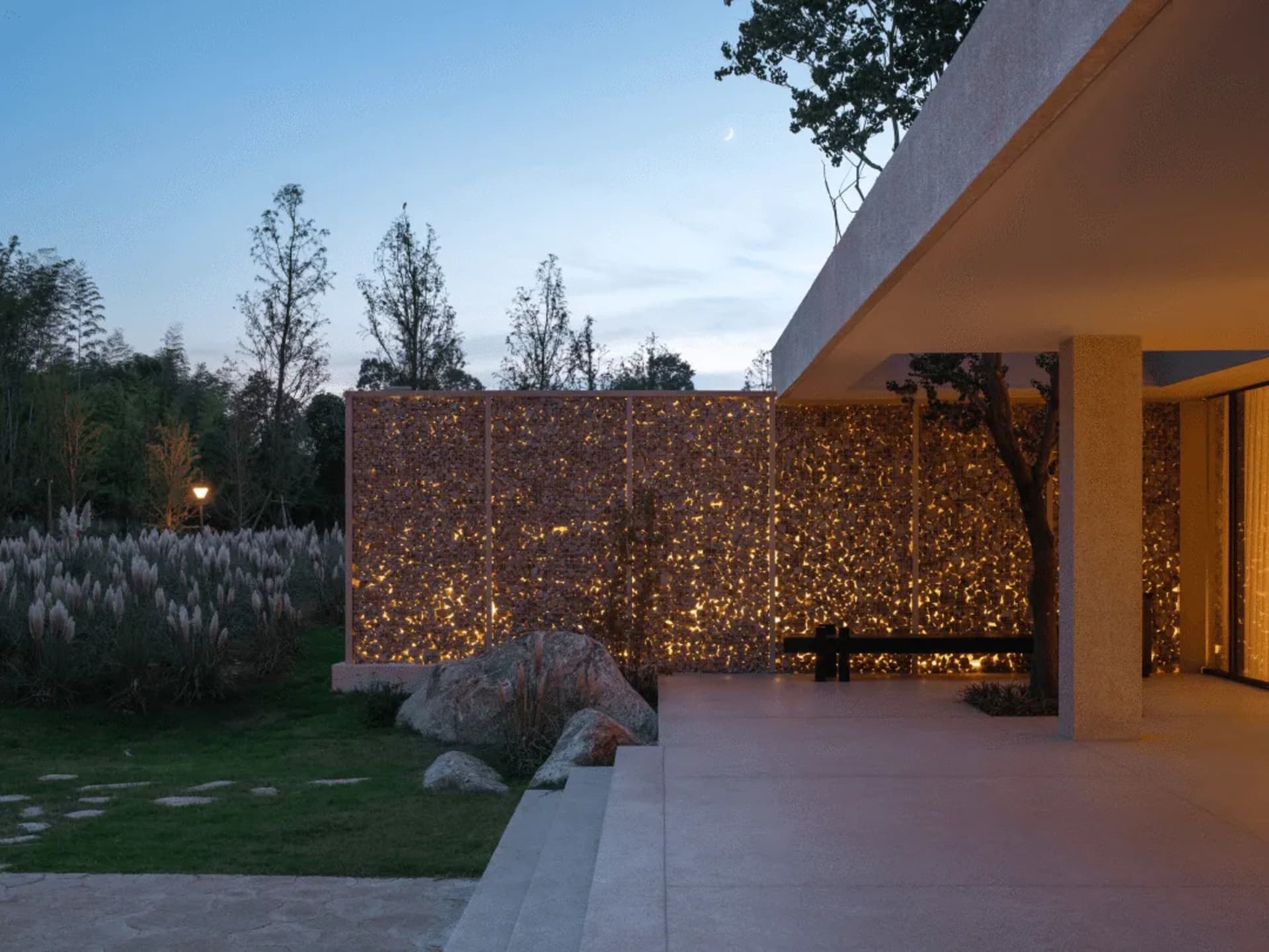 A well-lit photograph of a modern building with a bench and a tree in front of it, situated in a garden or public space