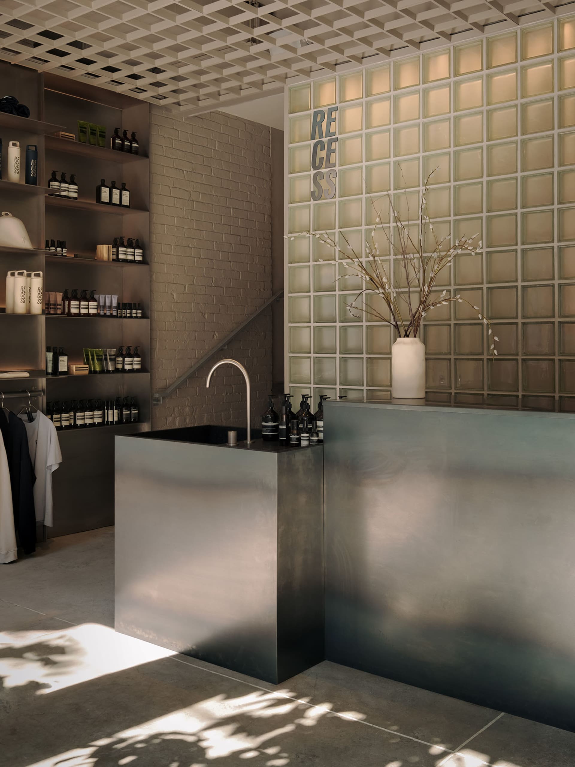 Bathroom with a metal sink, a potted plant, and a vase on a brick wall, with dim lighting creating a cozy atmosphere