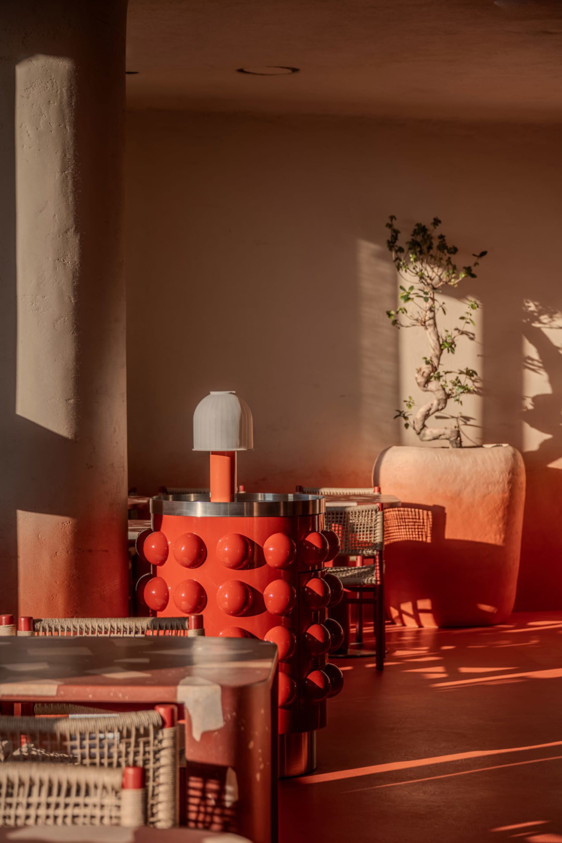 Cozy dining space with red walls, wooden furniture, and a potted plant, lit by dim lighting