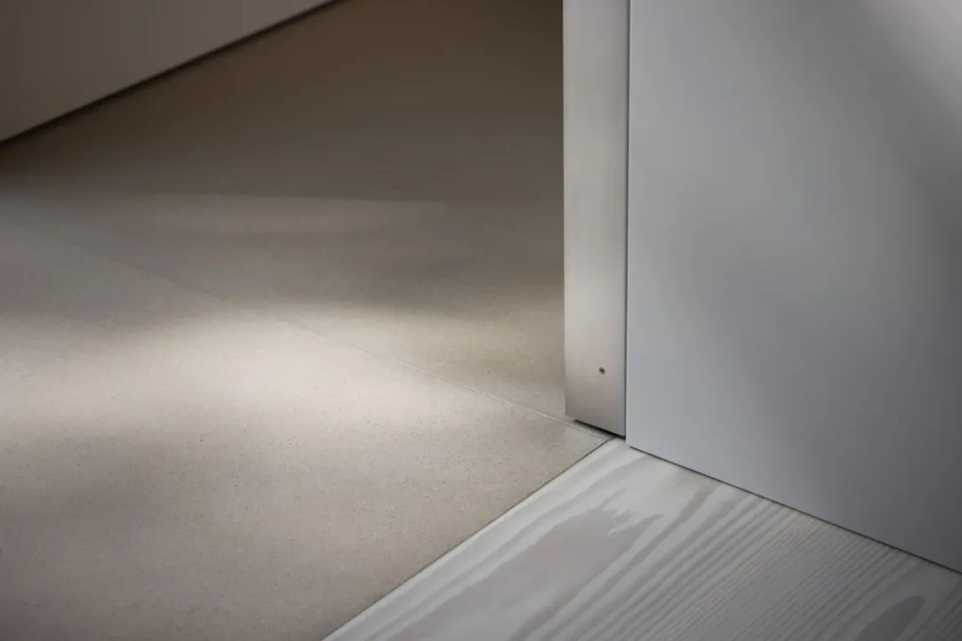 A small residential hallway with a wooden floor and a doorway leading to a view of the hallway, lit by natural light from the doorway