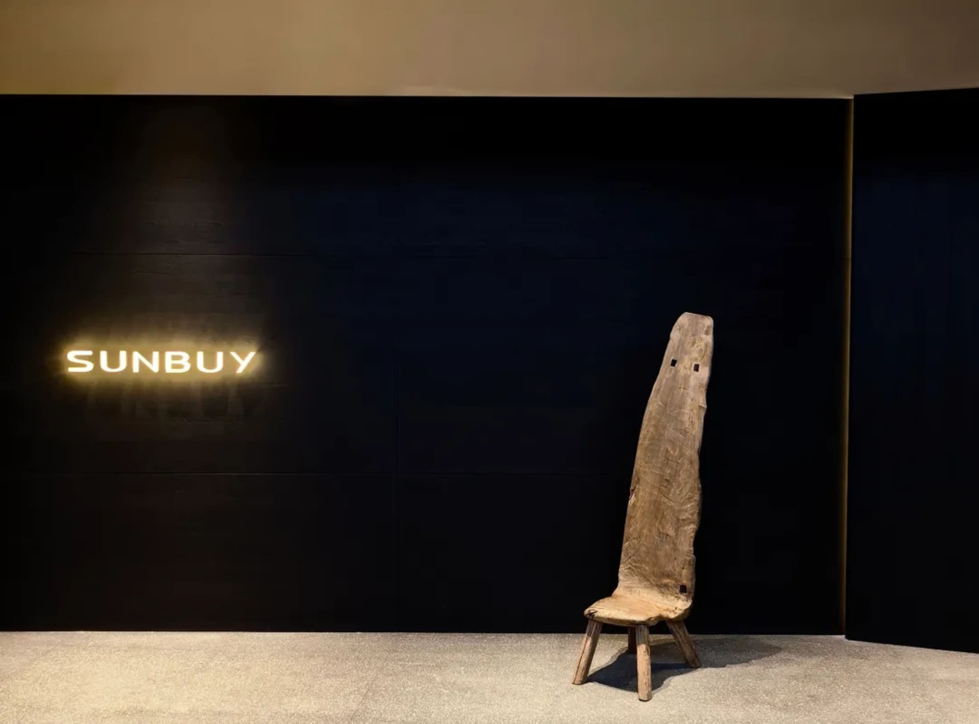 A modern living space with a wooden chair in front of a black wall, on a wooden floor, with a calm and inviting atmosphere