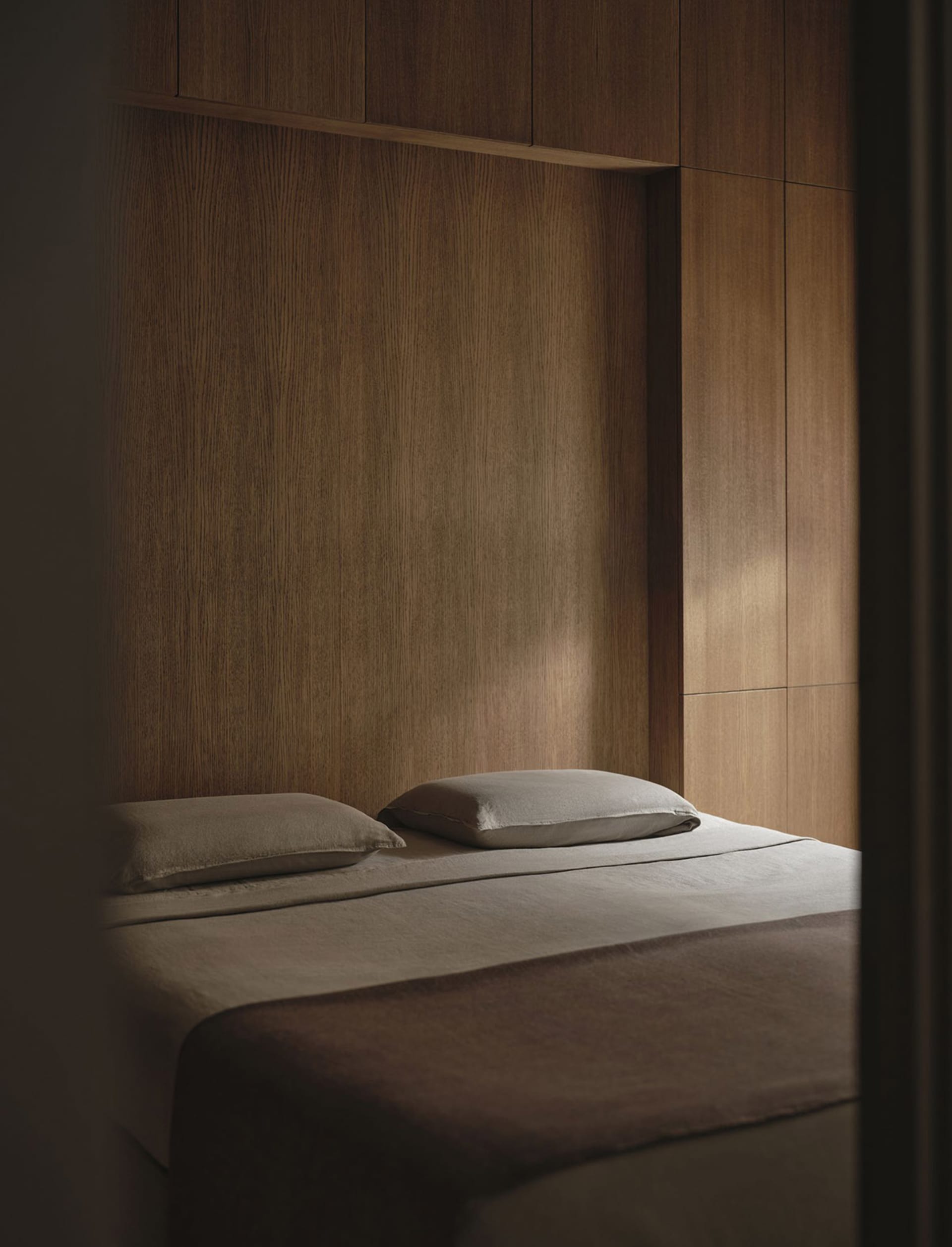 Cozy bedroom with a brown wooden wall, a white bed, and natural soft lighting