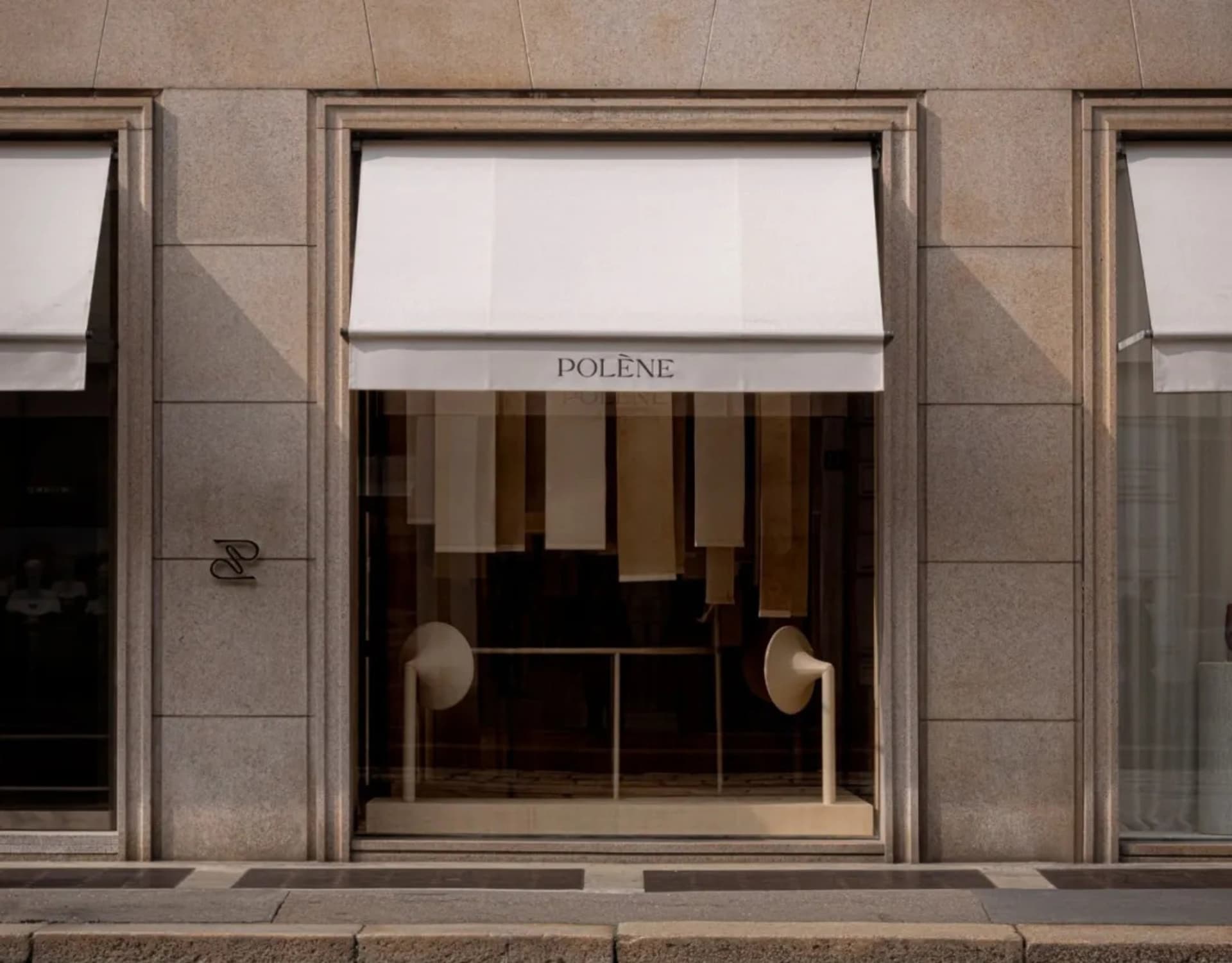 A classic storefront with a stone exterior, white awning, and window display featuring white curtains and a table, set against a bright and welcoming background