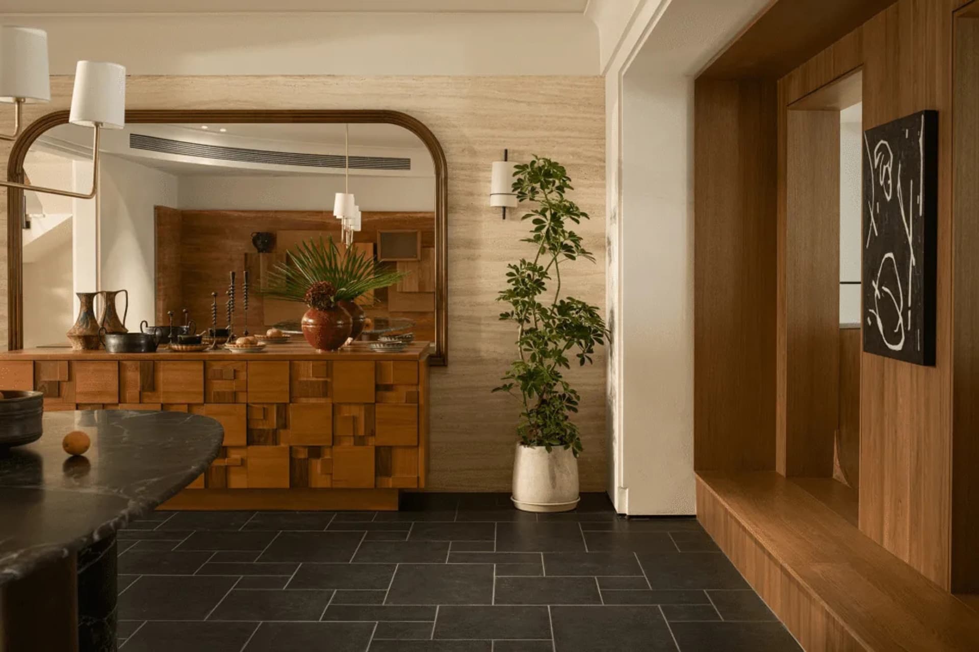 Cozy kitchen with a wooden floor, black countertop, and natural materials, featuring a sink, potted plant, and vase, with dim lighting