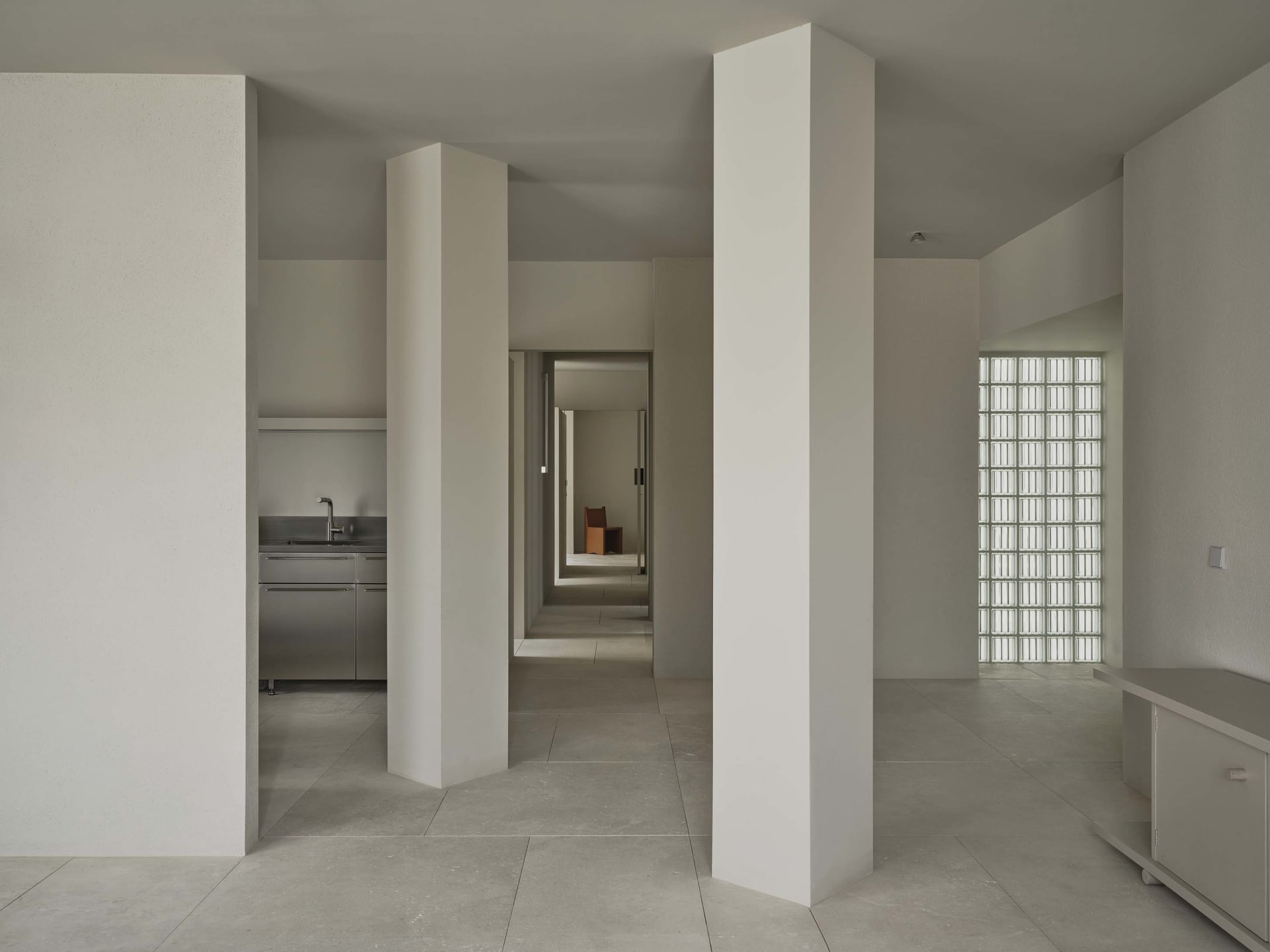 A bright and inviting kitchen and hallway with white walls, tile floors, and natural light from windows