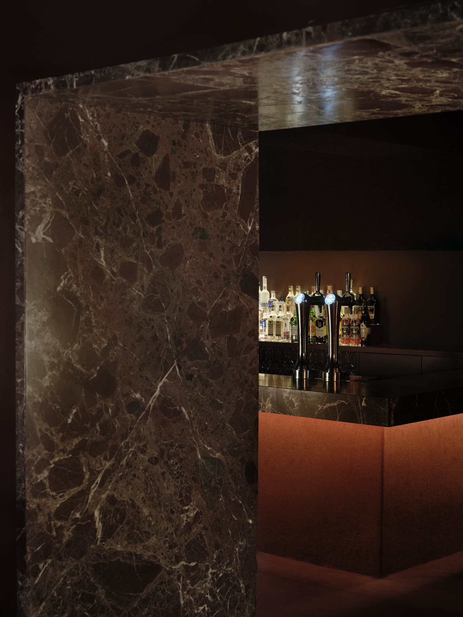 A modern bar with a marble countertop featuring various bottles arranged in a visually appealing way, set in a well-lit environment