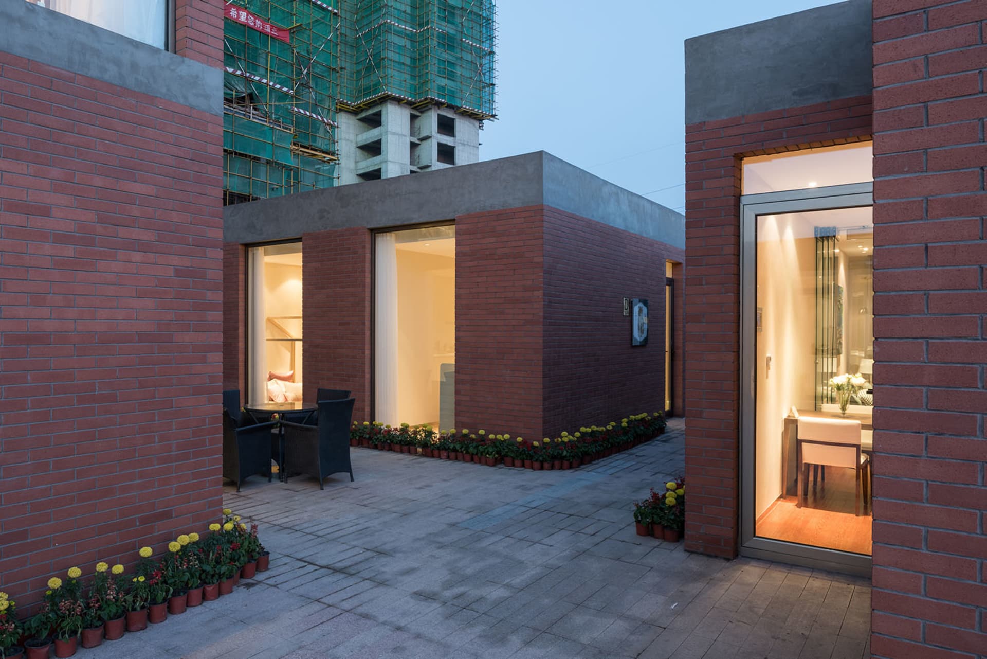 A modern living space with a brick exterior, large window, and a well-lit interior with a dining table and chairs