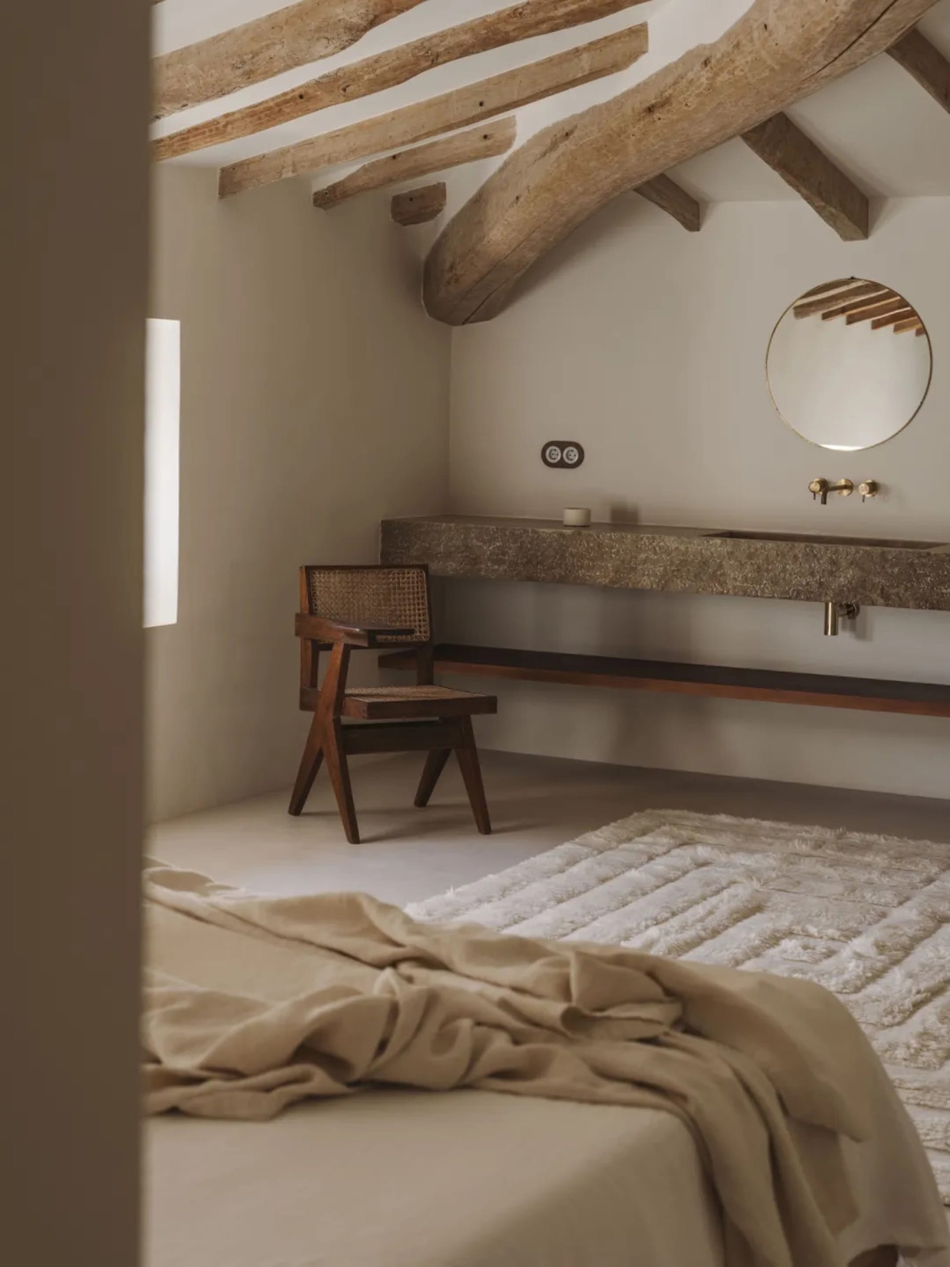 Cozy bedroom with a wooden bed, chair, and sink, featuring a white blanket and wooden walls
