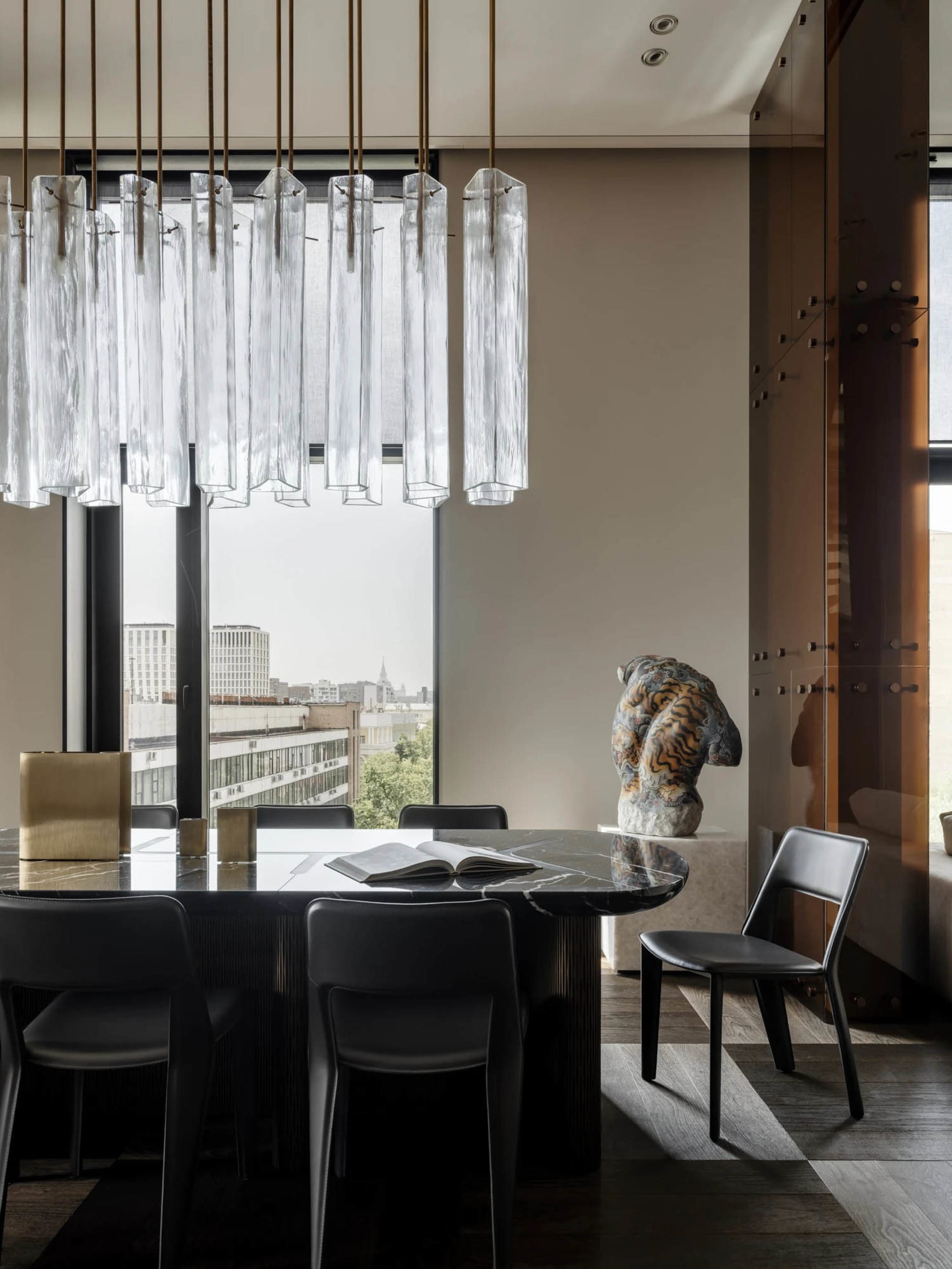 Cozy modern living space with a dining table, couch, and chandelier, surrounded by wood and glass materials in a dimly lit atmosphere